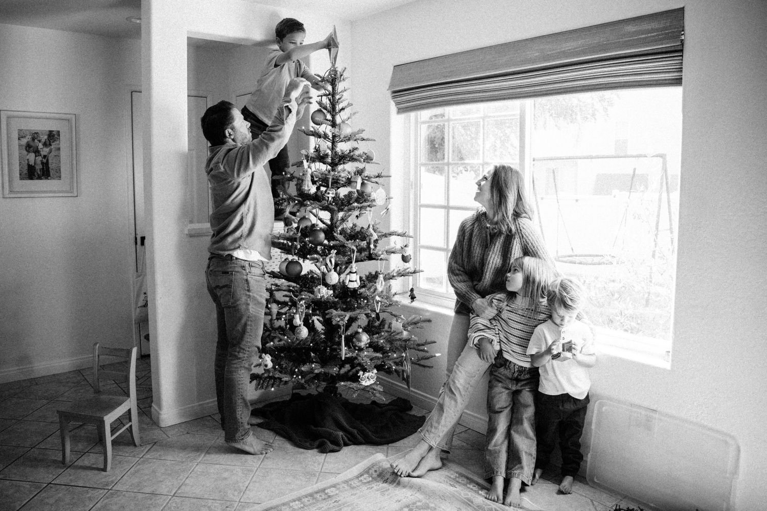 Black and white photo of a family decorating a Christmas tree together in their living room.