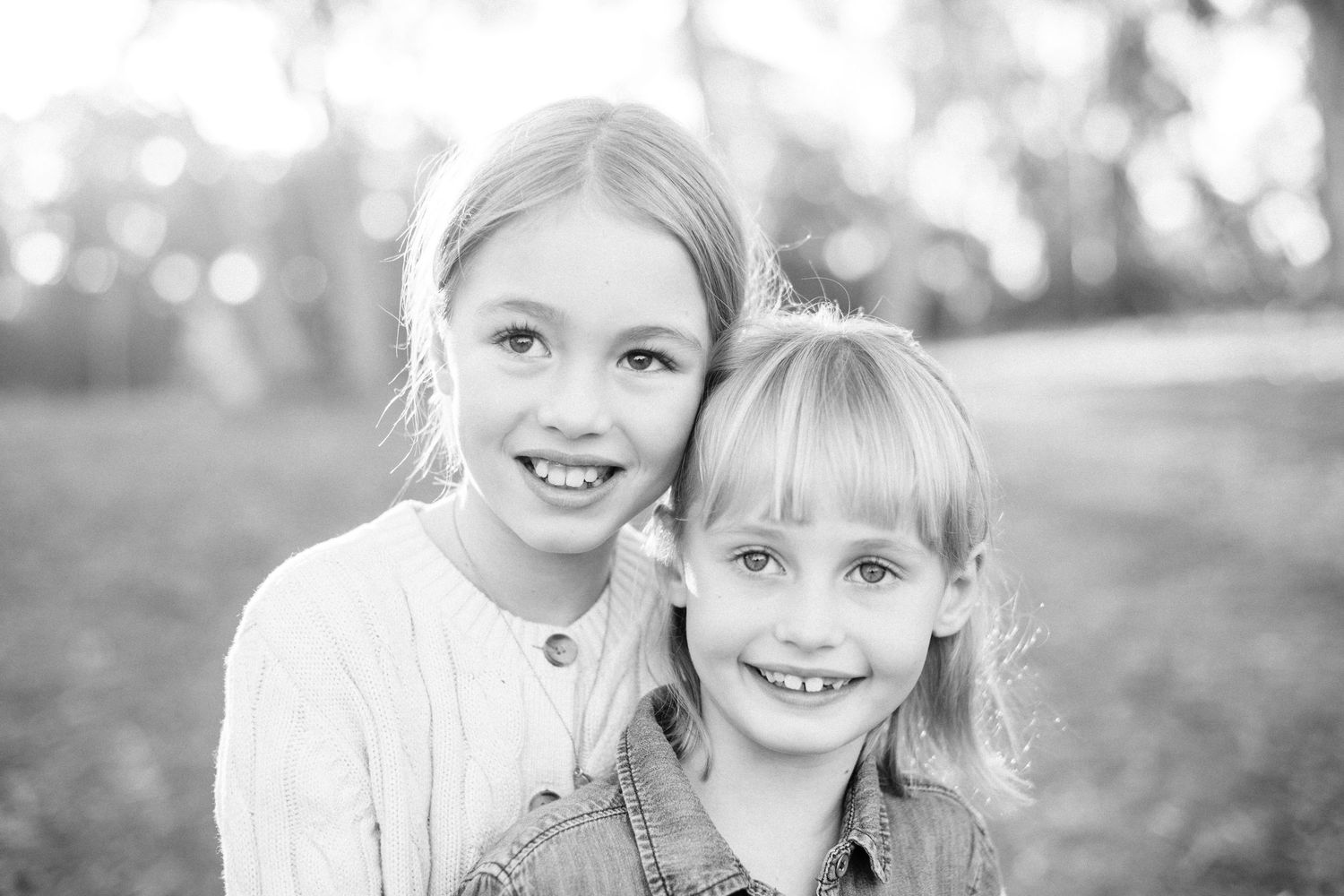 Black and white portrait of two smiling young girls posing together outdoors in a park setting.