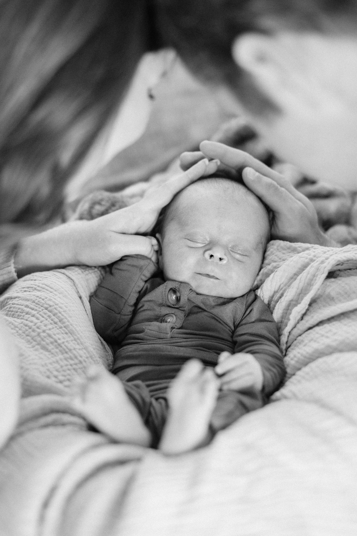 Black and white close-up of a sleeping newborn baby cradled gently in a parent's hands on a soft blanket.