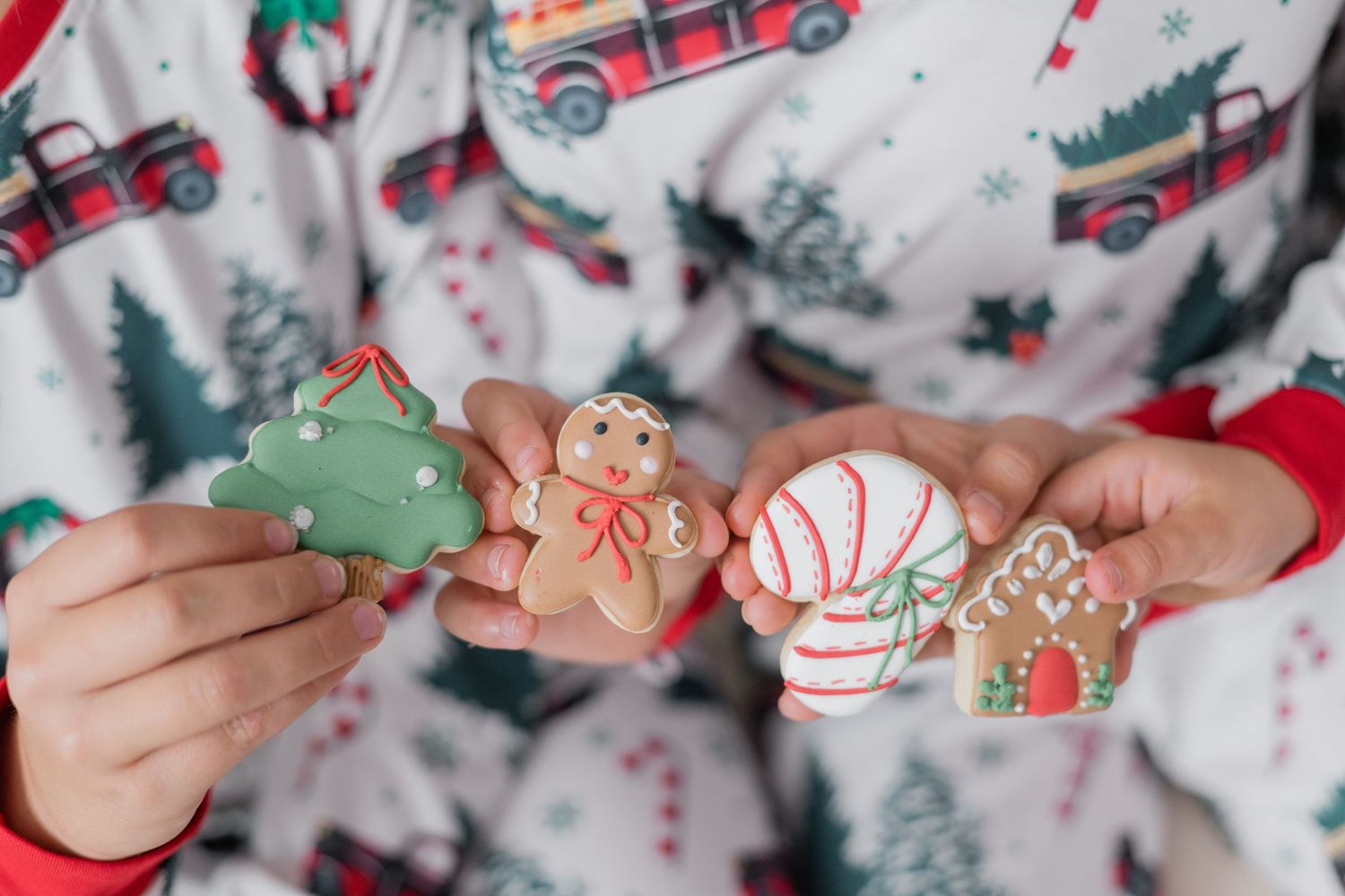 Child in Christmas pajamas holding festive decorated gingerbread cookies including a tree, man, ornament, and house.