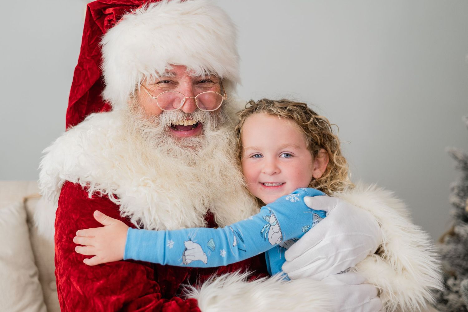 A cheerful child hugs Santa Claus, both smiling warmly during a festive Christmas photo session.