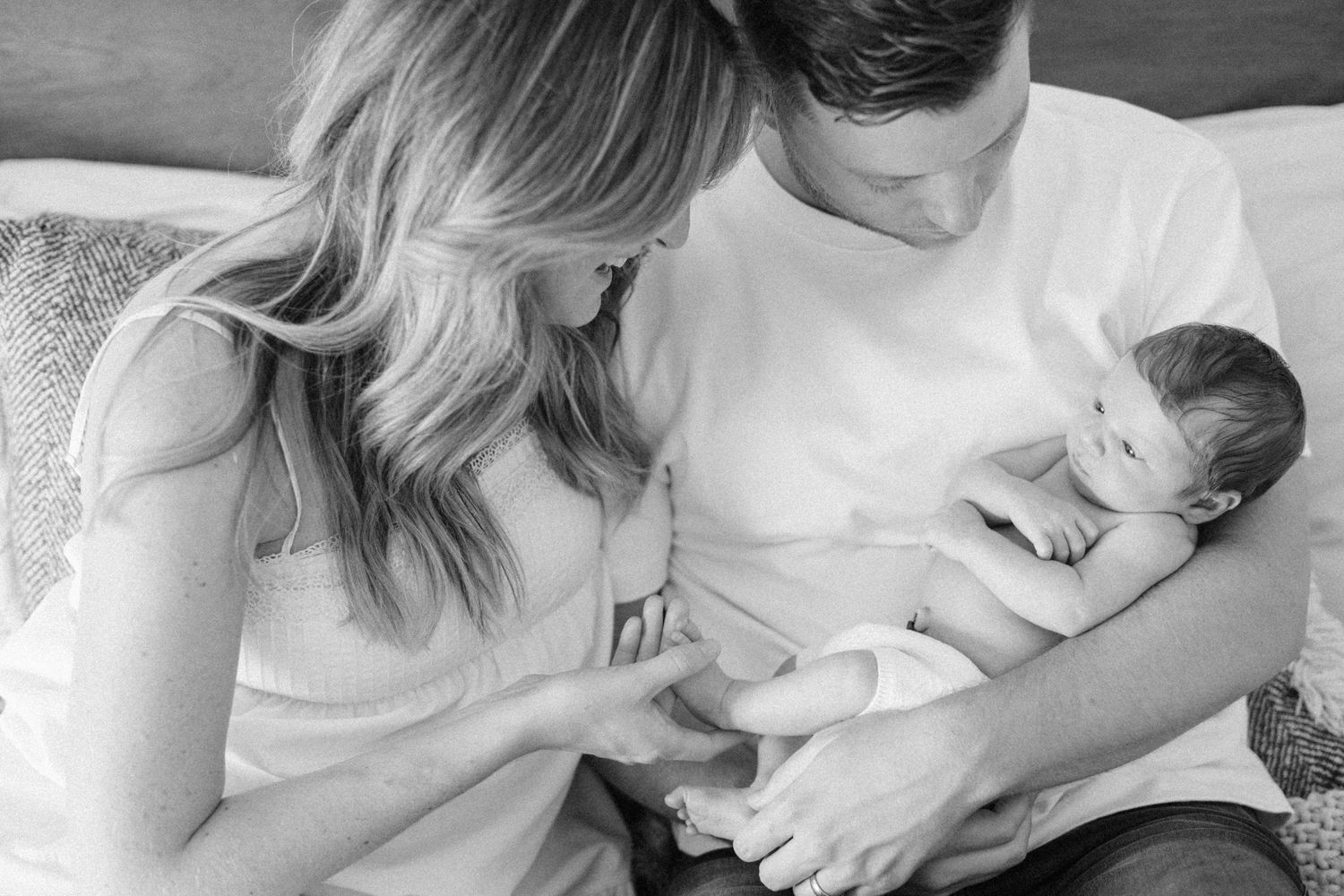 Black and white photo of parents lovingly gazing at their newborn baby together.