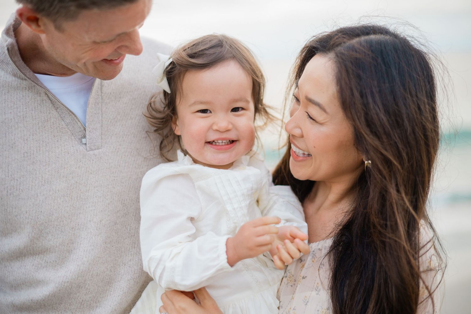 Happy family portrait with parents holding smiling toddler girl on a beach.