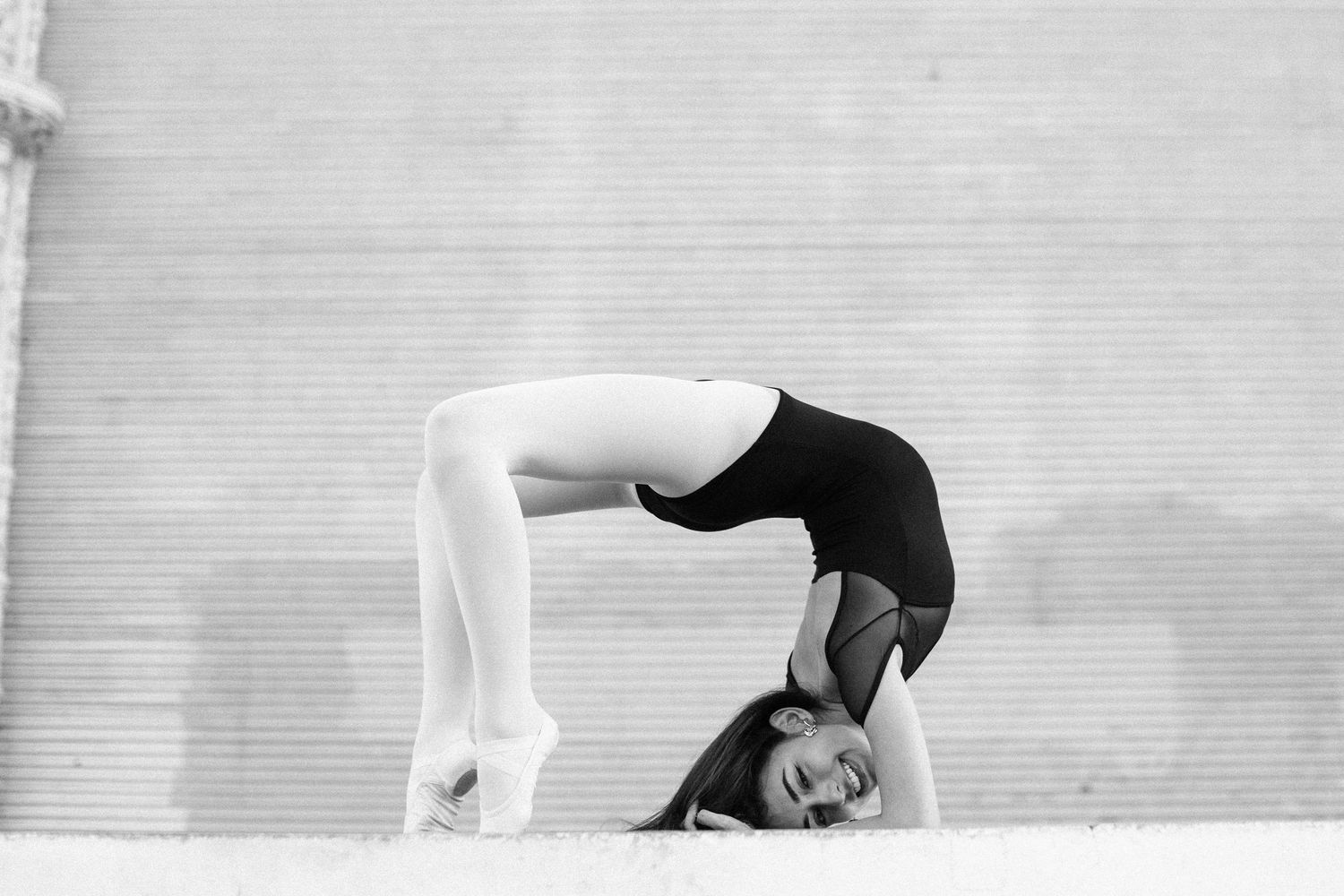 Black and white photo of a flexible gymnast performing a backbend on the ground outdoors.