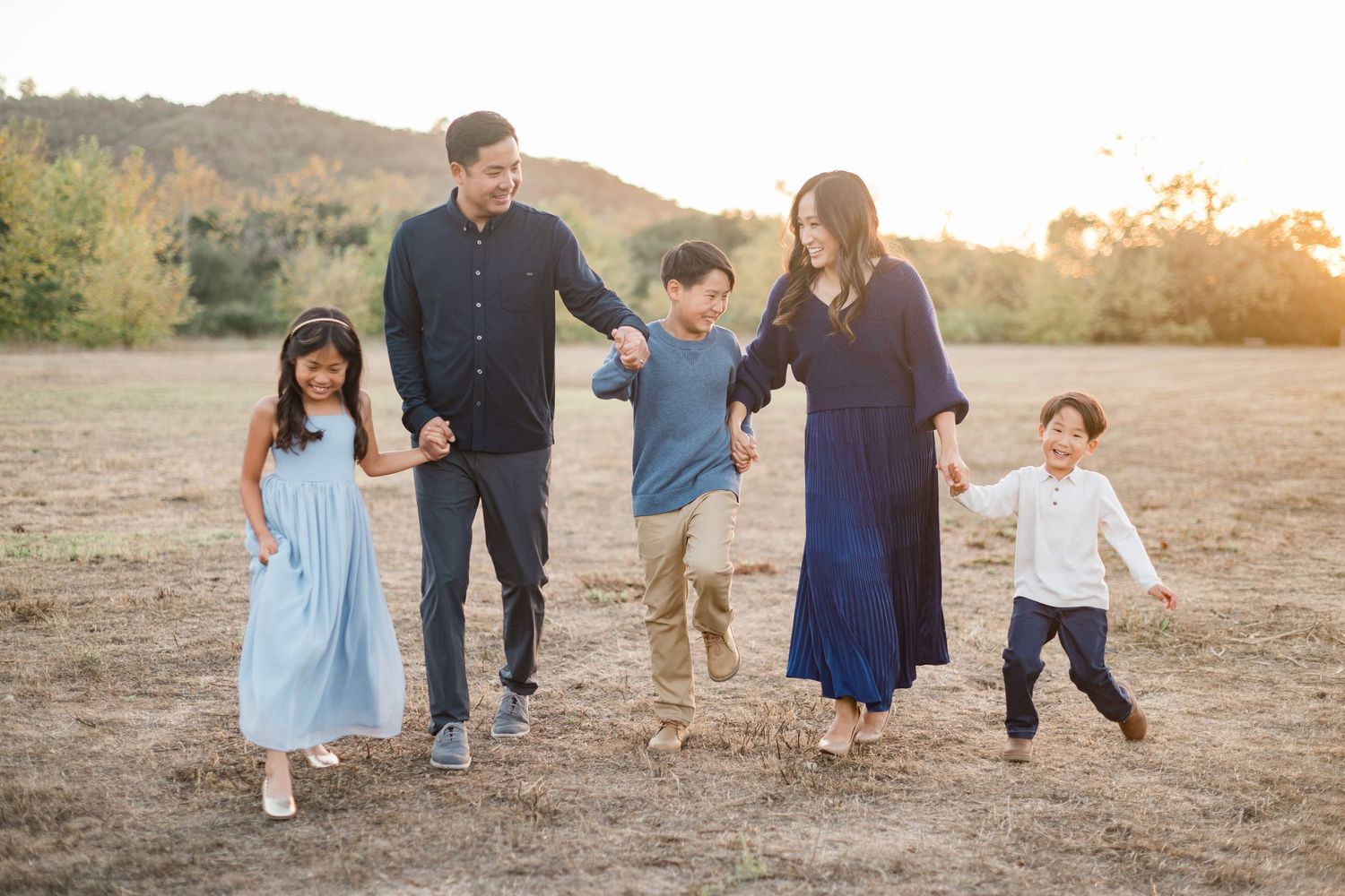 Family of five holding hands walking in a sunny field during golden hour outdoor photo session.