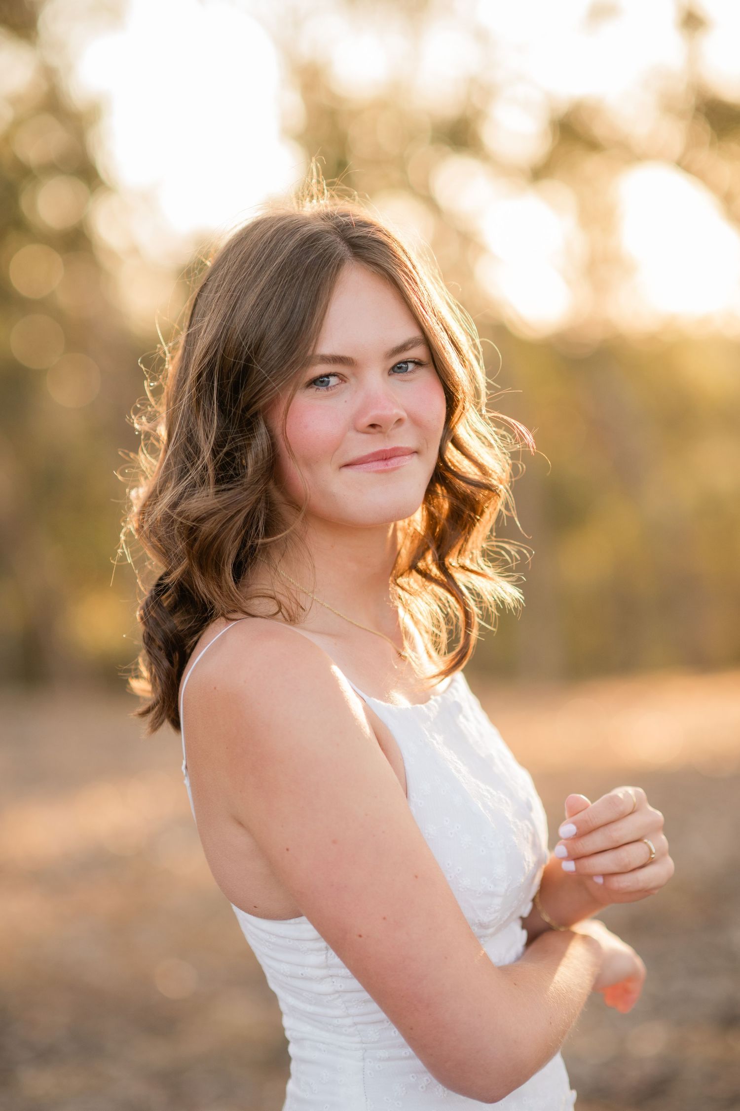 Young woman in white dress smiling over shoulder in golden hour sunlight outdoors.