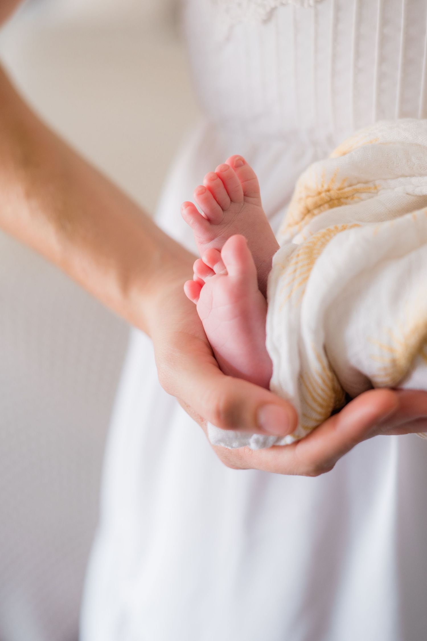 Close-up of tiny newborn baby feet resting gently in a mothers hands wrapped in a soft blanket.
