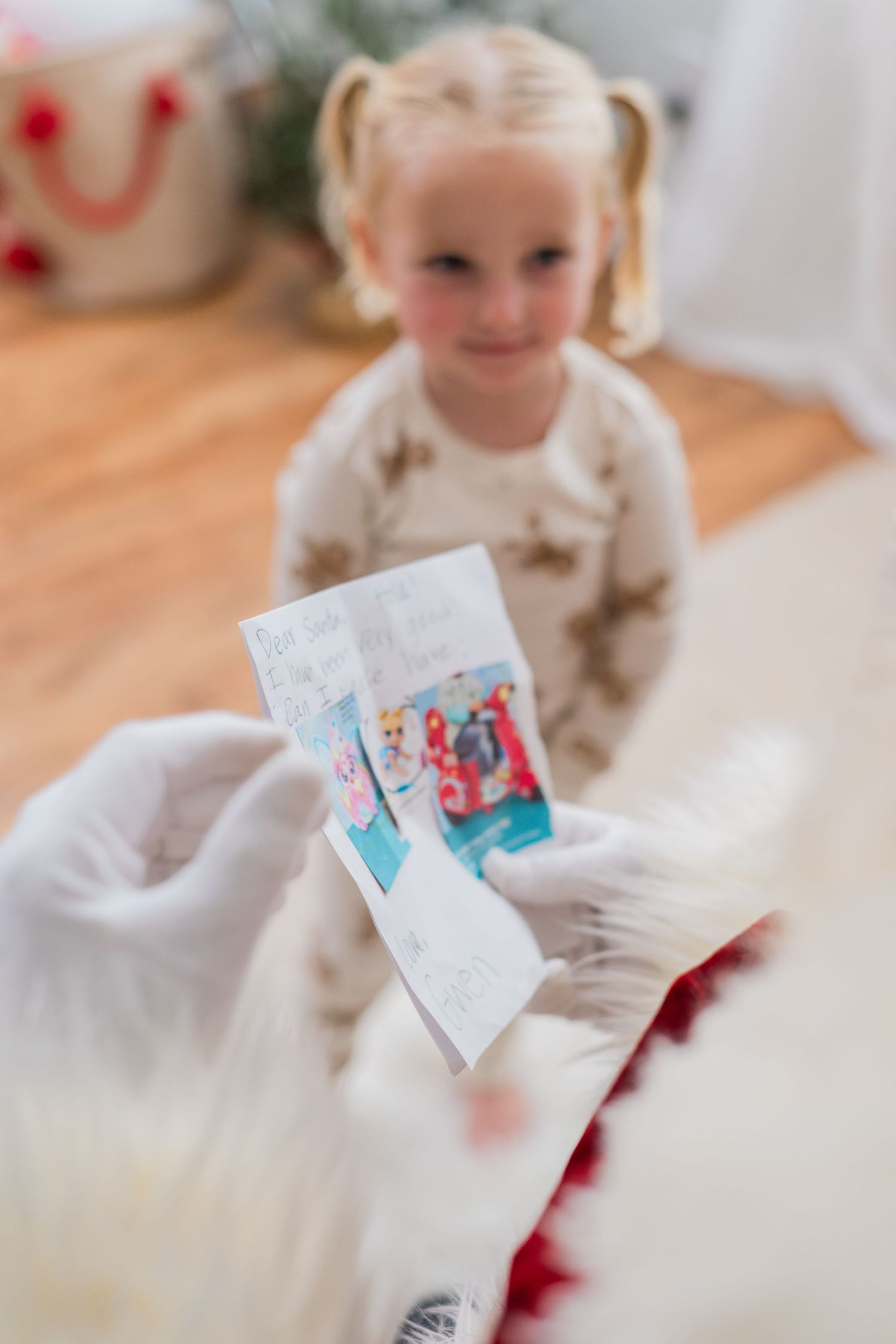 Young blonde girl in pigtails smiles as Santa Claus reviews her handwritten Christmas wish list.