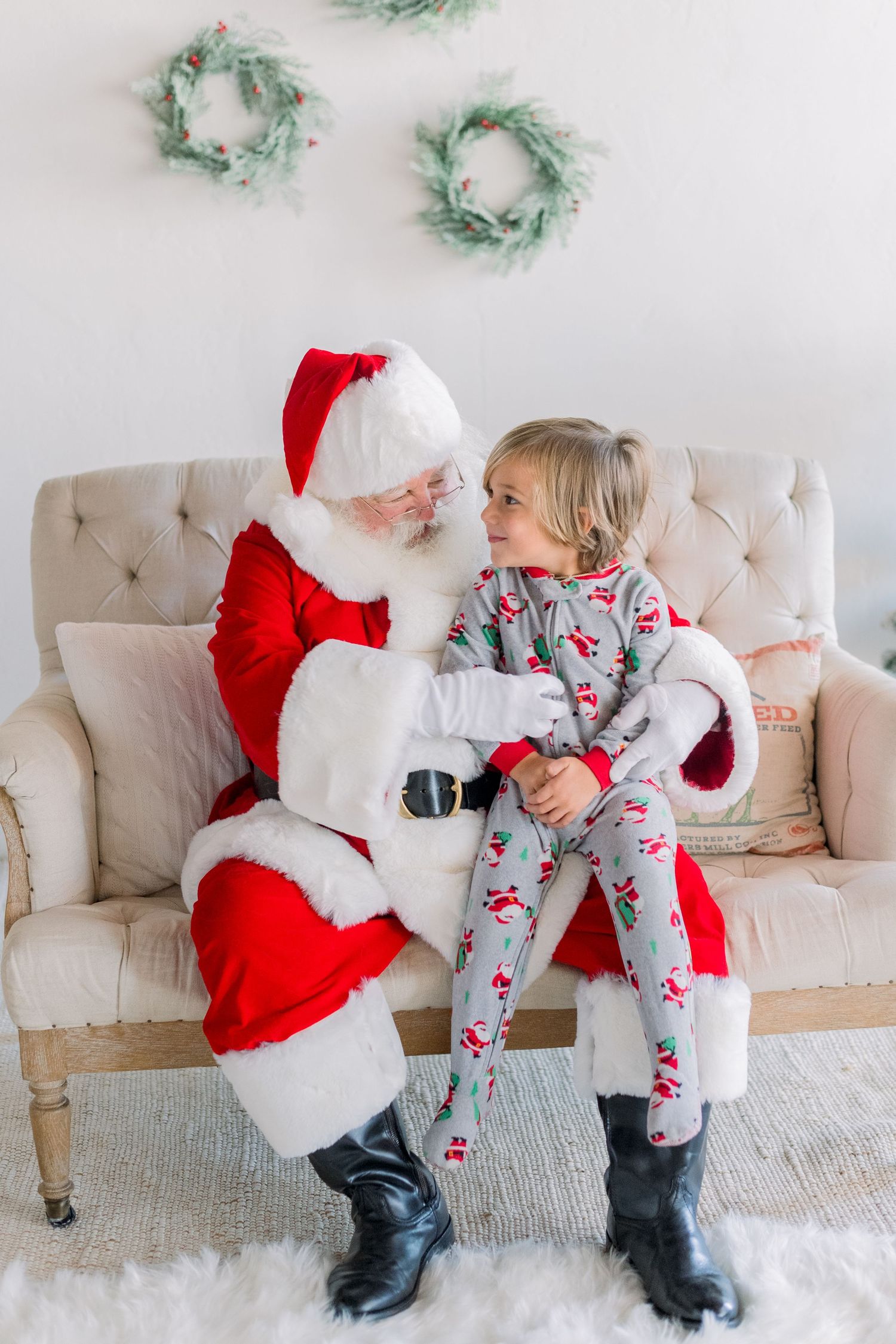 A little girl in festive pajamas sits on Santa's lap, smiling up at him during a Christmas photo session.