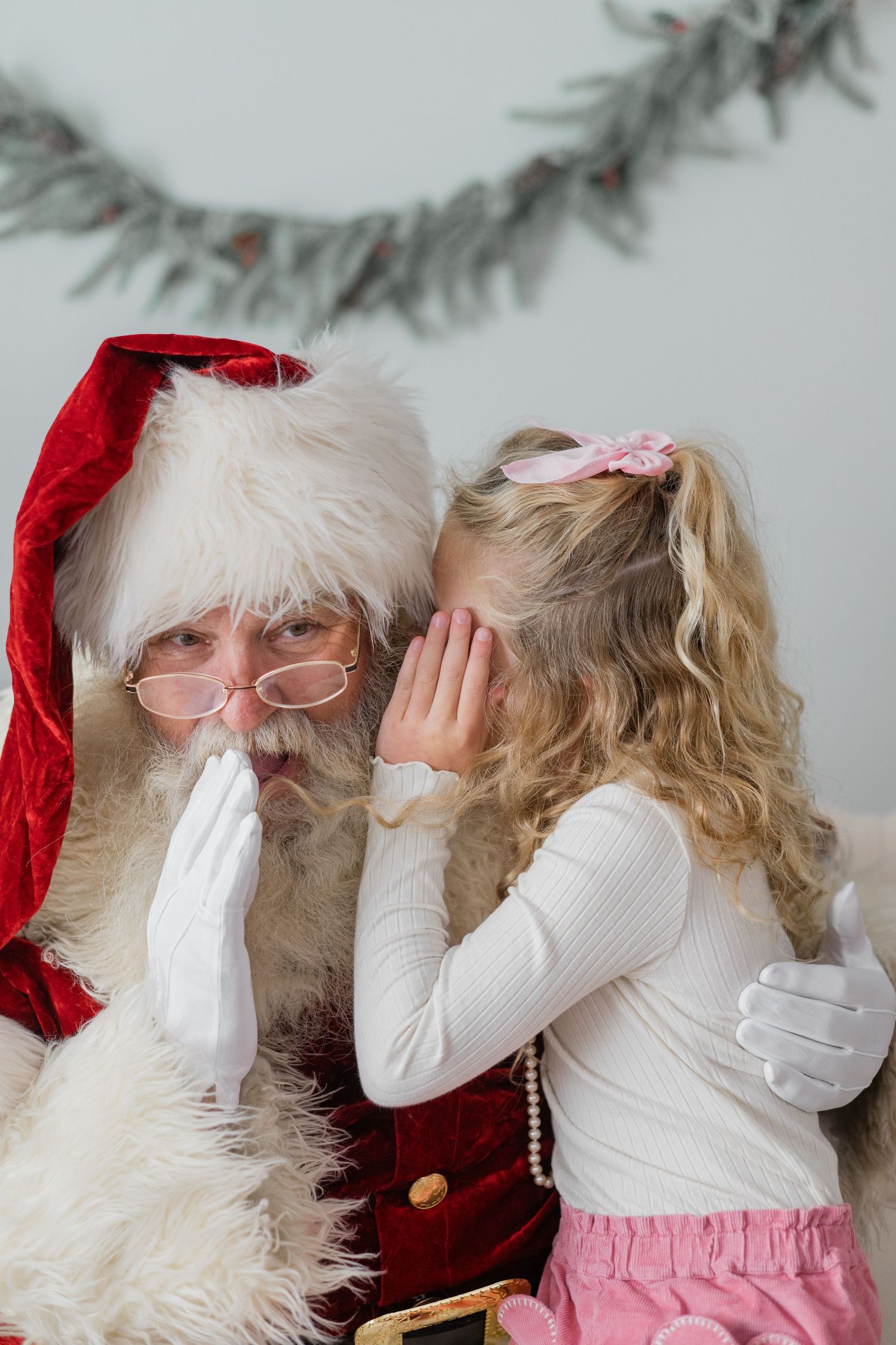 A young girl whispers her Christmas wishes into Santa Claus's ear during a festive holiday photo session.