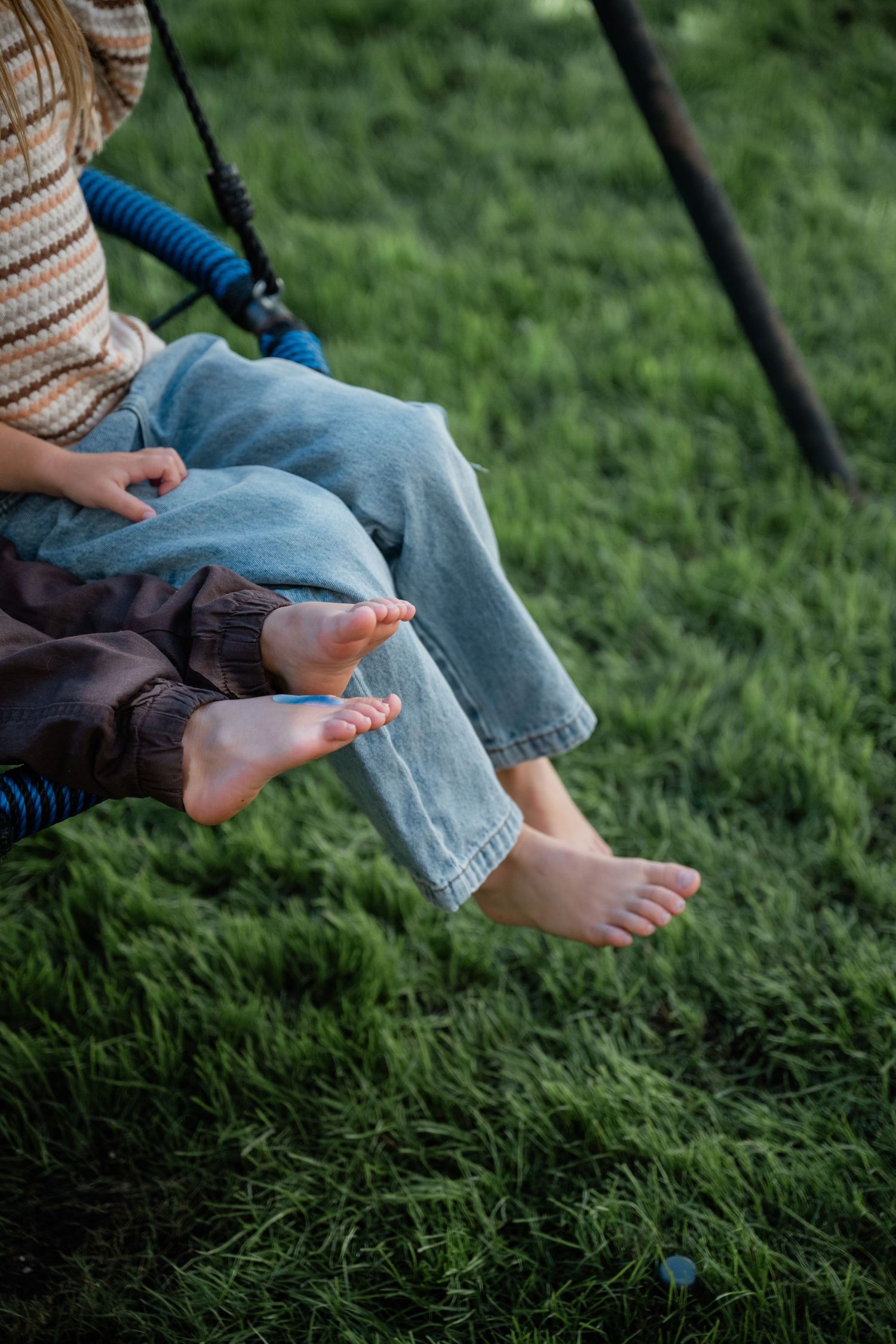 Close-up of children's bare feet dangling from a blue rope swing over lush green grass.