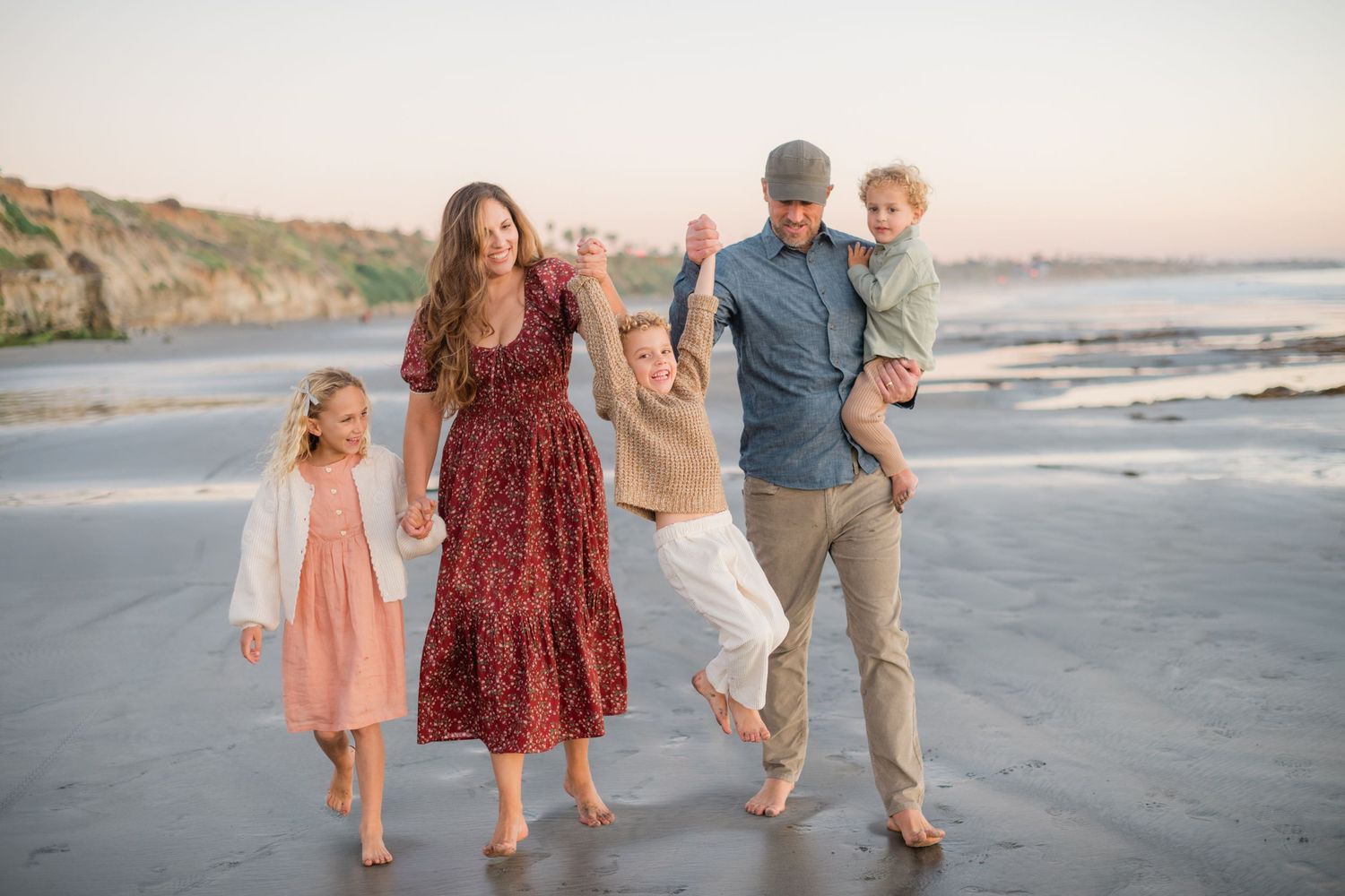 Family of five walking and playing on a sandy beach at sunset, with cliffs in the background.