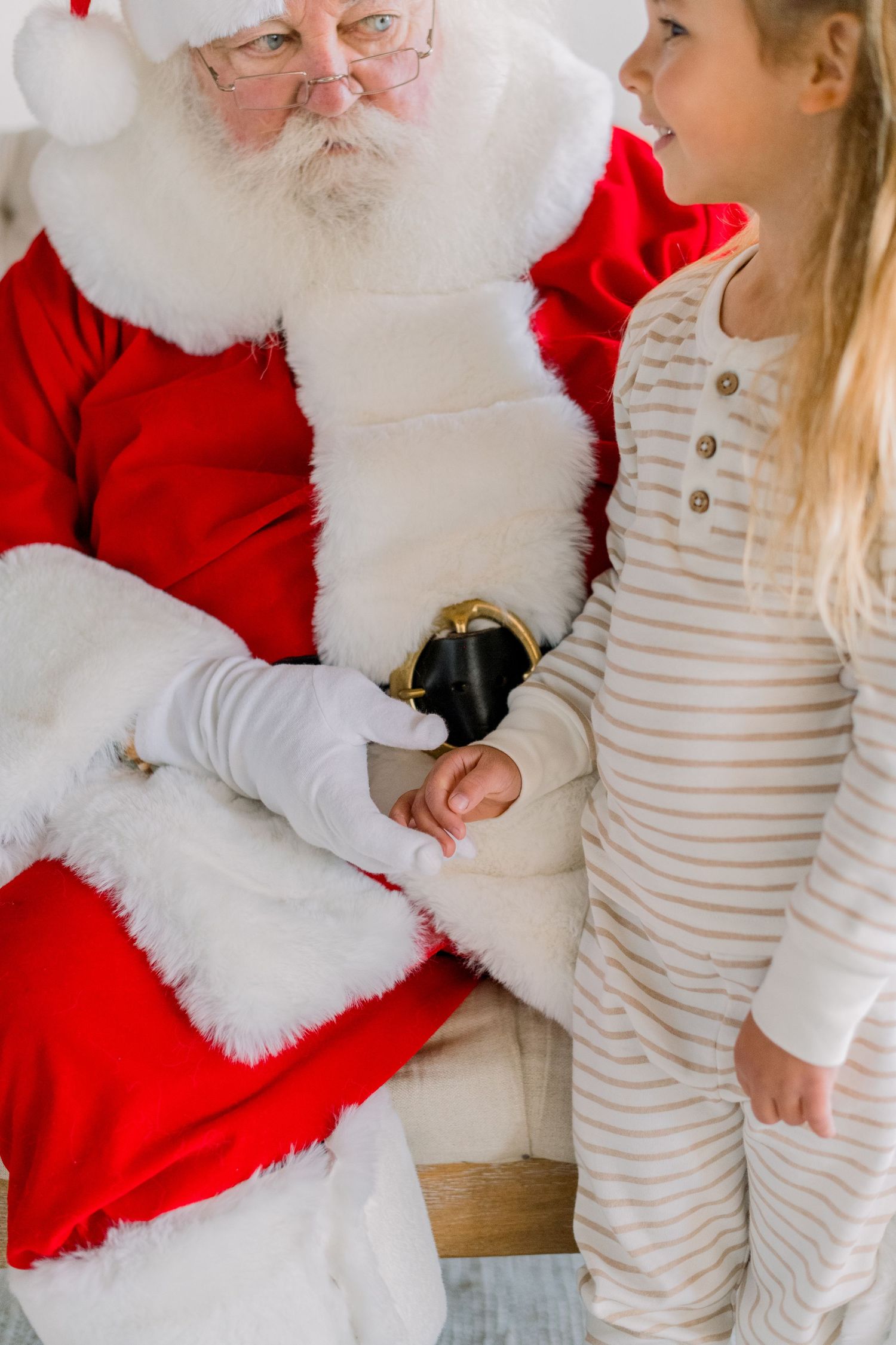Young girl in striped pajamas holding Santa Claus's hand during a festive Christmas photo session.