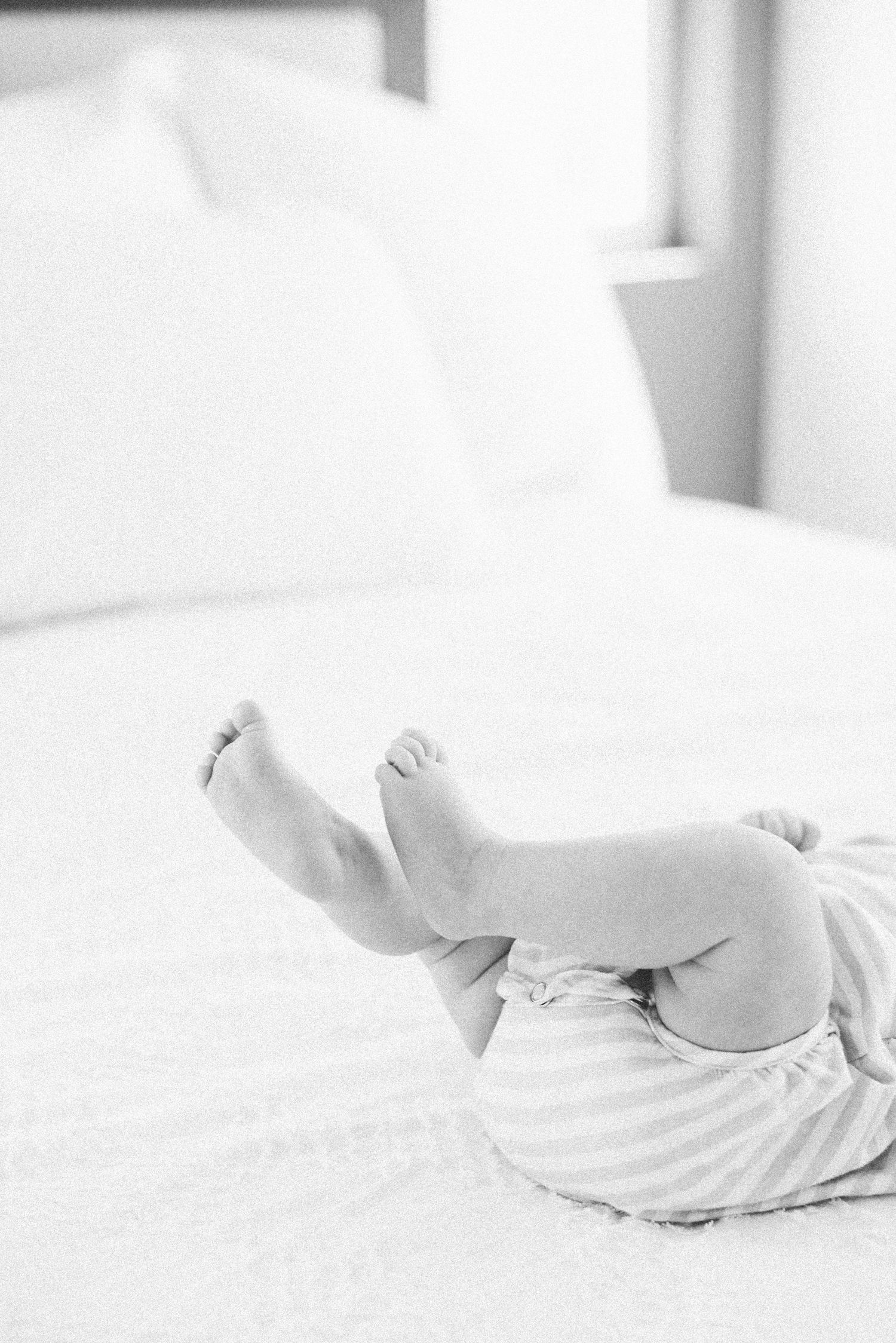 Adorable newborn baby lying on white bed with tiny feet raised in the air wearing striped pants.