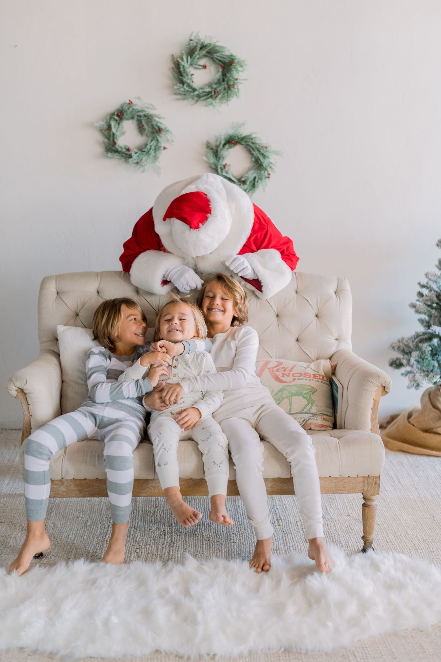 Three children in pajamas sit on a couch with Santa Claus during a festive Christmas photo session.