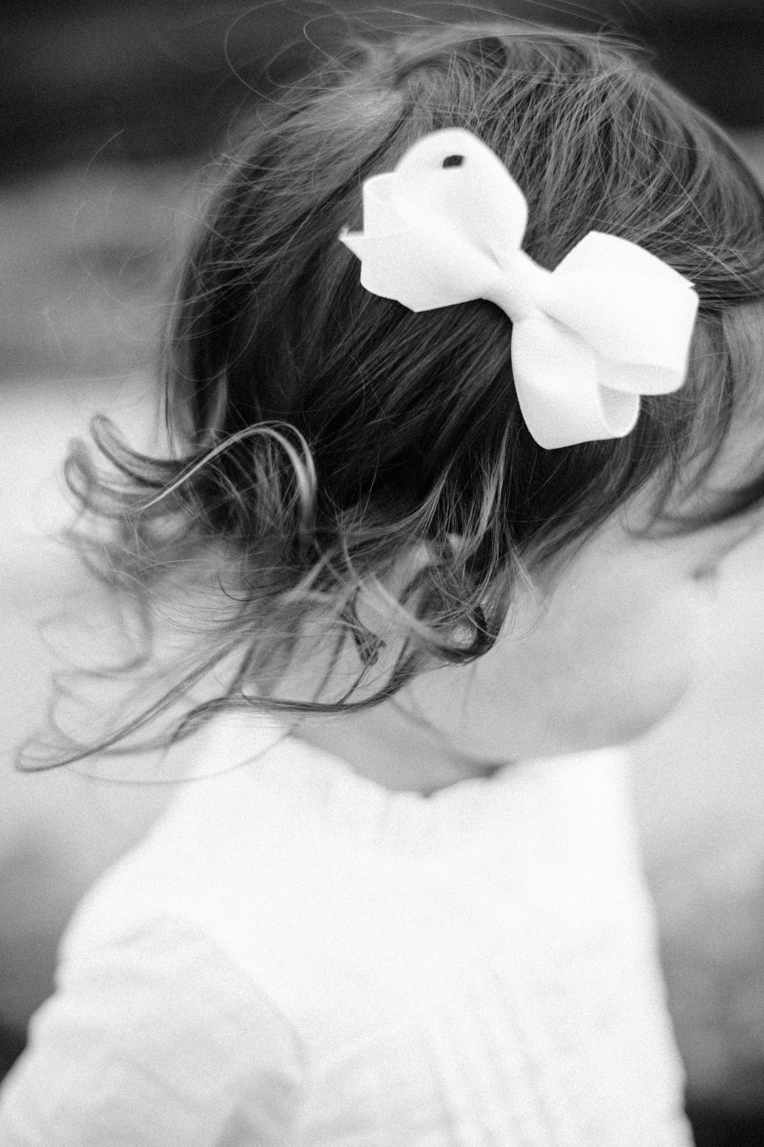 Black and white portrait of a young girl with a white bow hair clip in her dark hair.