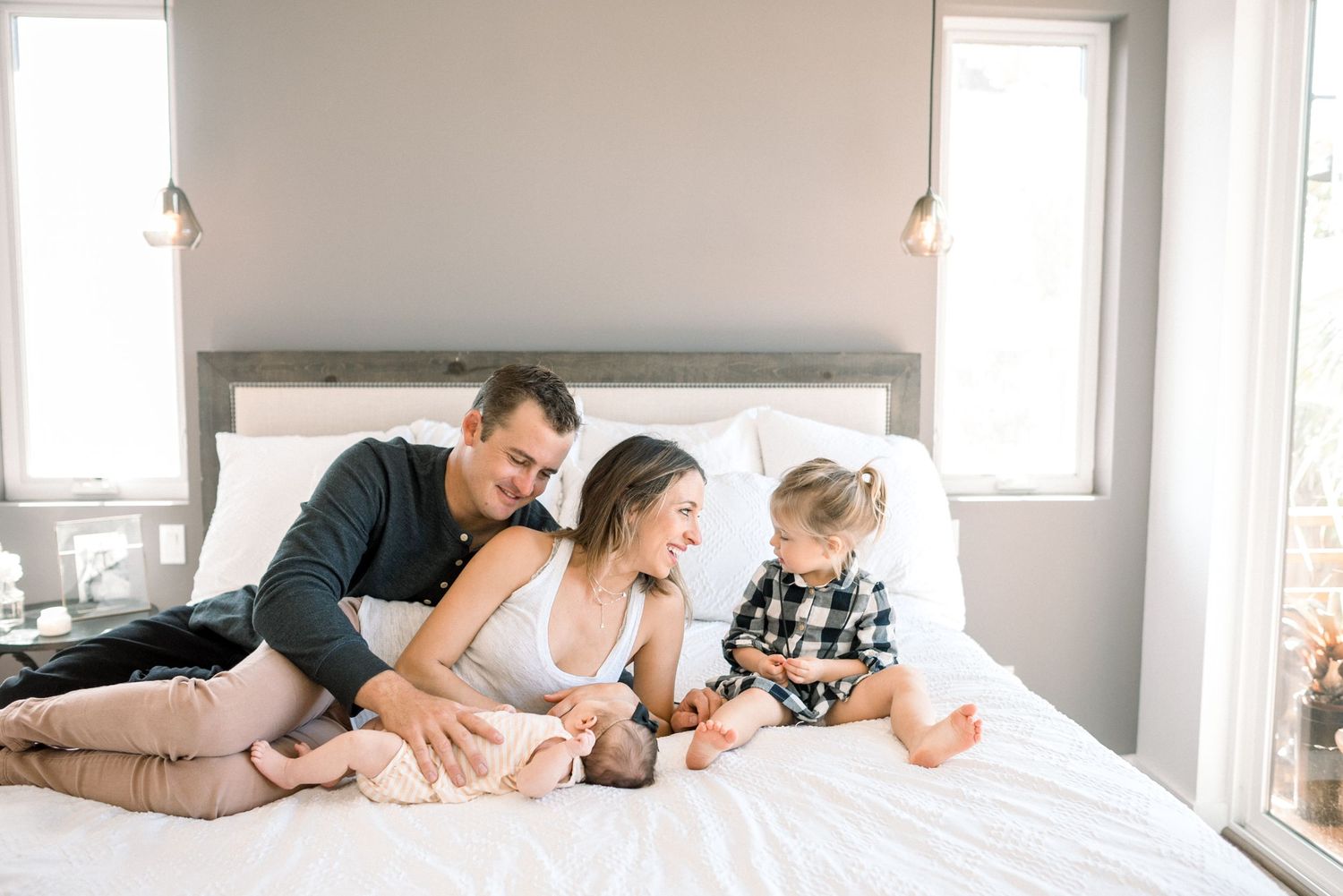 Happy family with newborn baby relaxing together on a white bed in a bright modern bedroom.