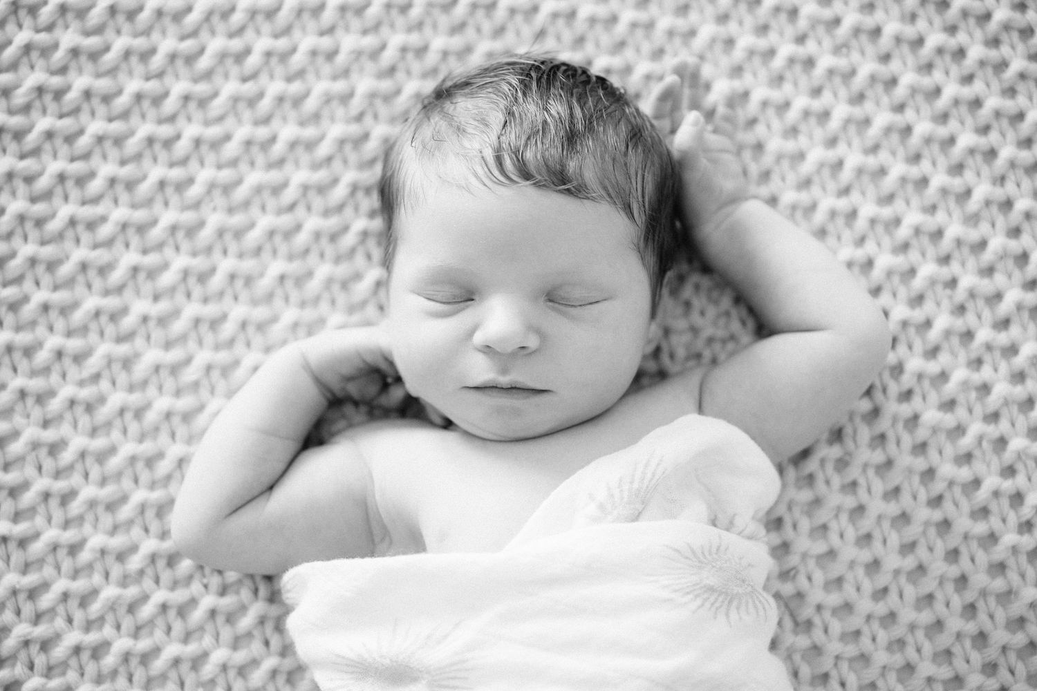 Black and white photo of peaceful sleeping newborn baby with hands behind head.