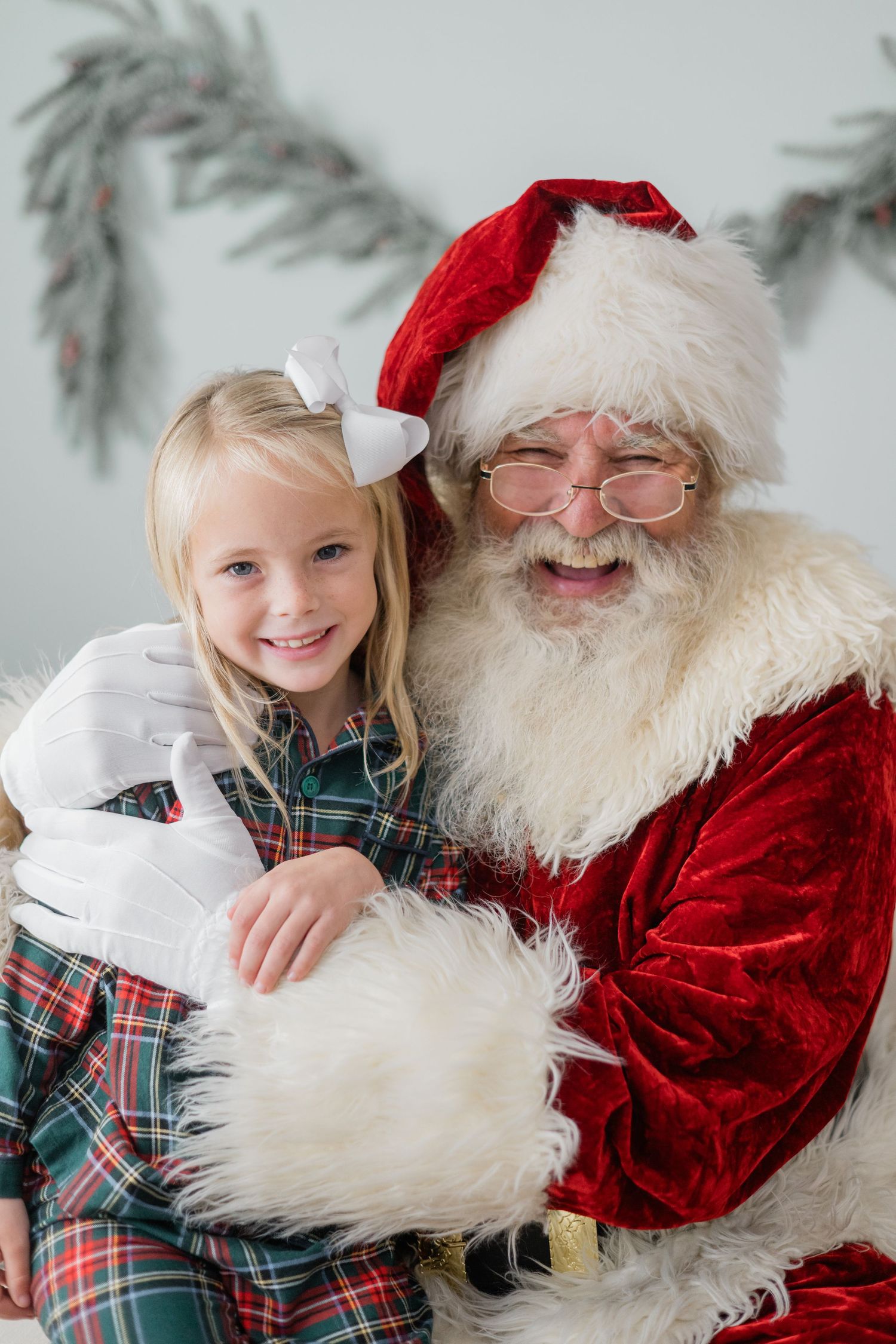 Young girl in plaid dress smiling with Santa Claus during a festive Christmas portrait session.