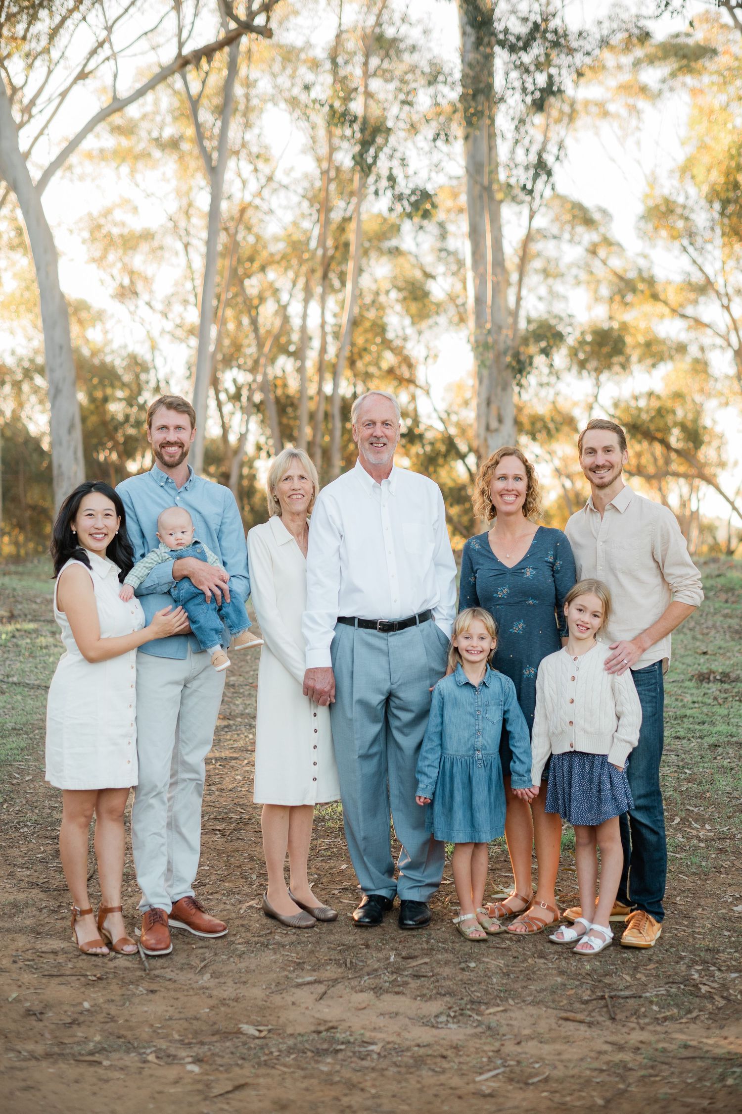 Multi-generational family portrait with grandparents, adult children, and grandkids in a sunny park.