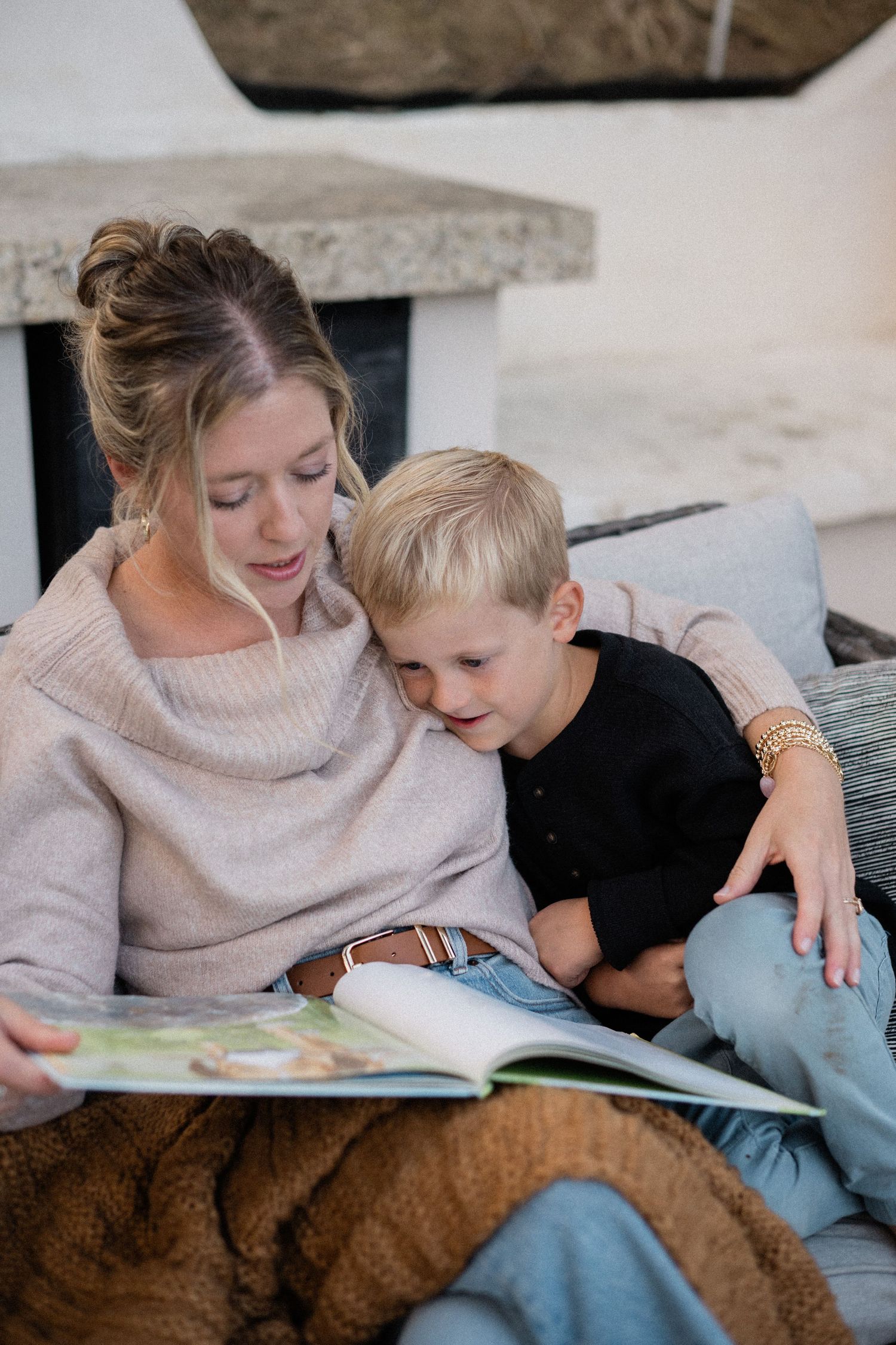 A mother reads a colorful picture book with her young son on a cozy sofa.