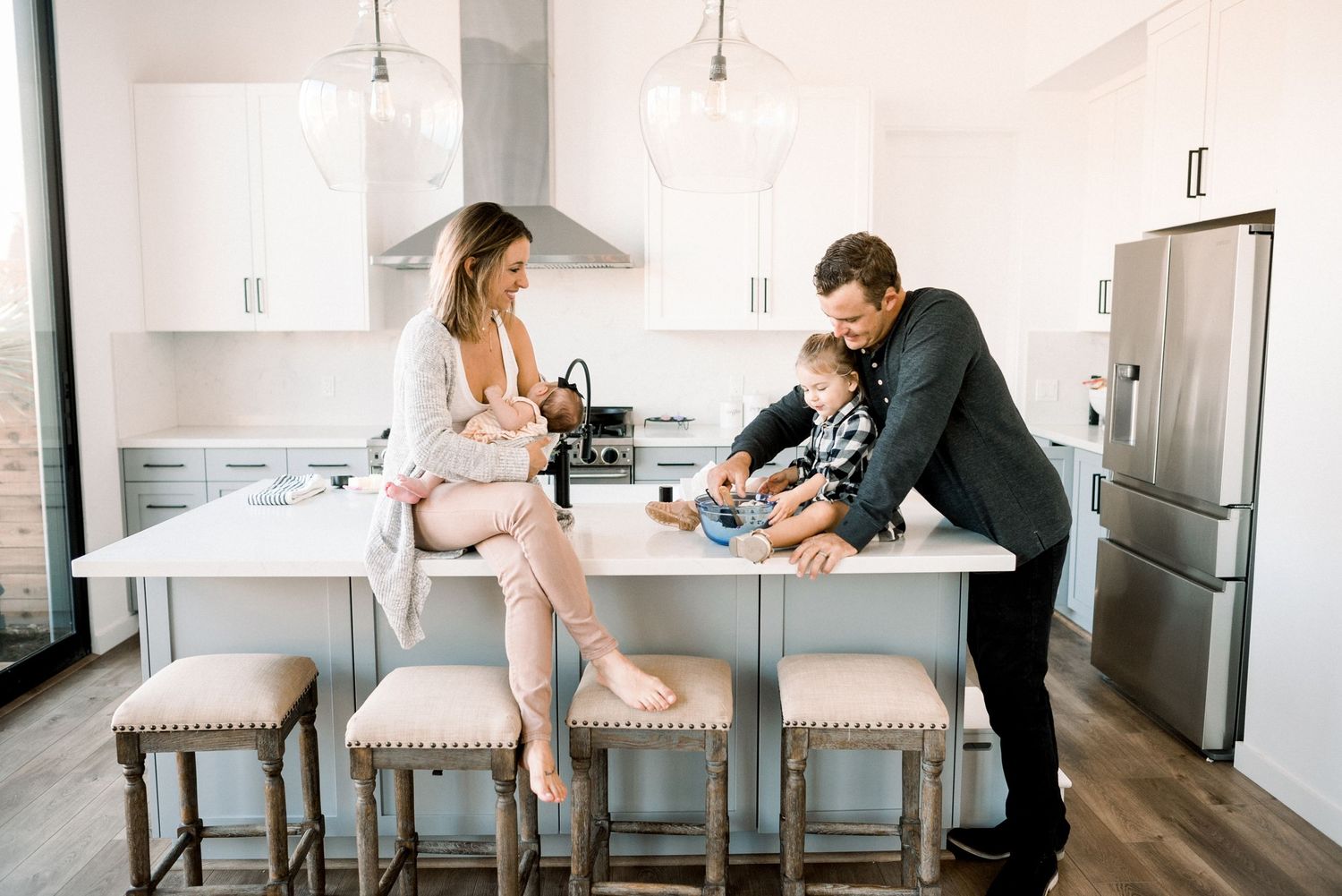 A happy family with a toddler gathered around a white kitchen island in a modern bright home.