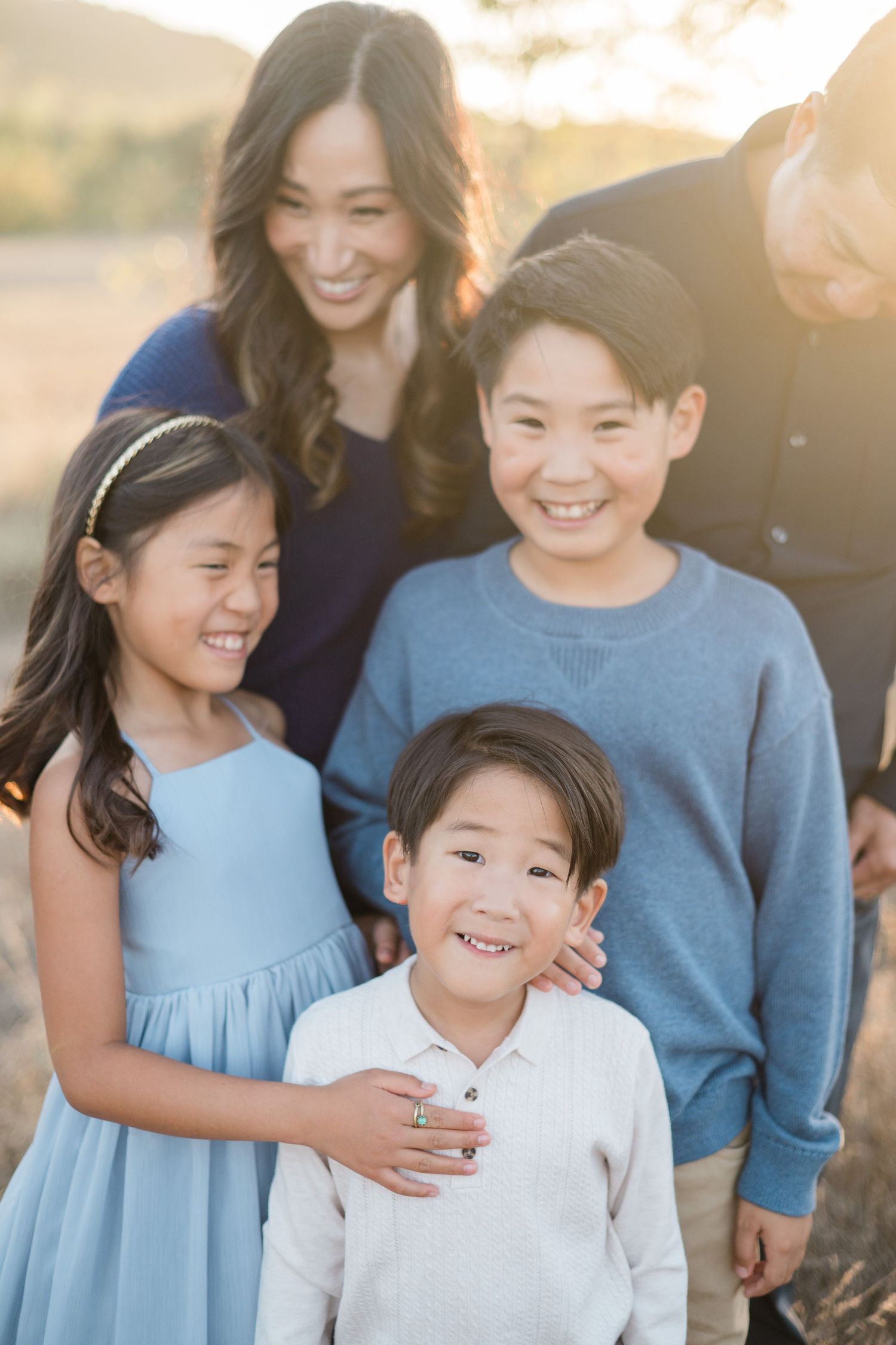 Close-up of smiling Asian family with mother and three happy children laughing together in a sunny outdoor setting.