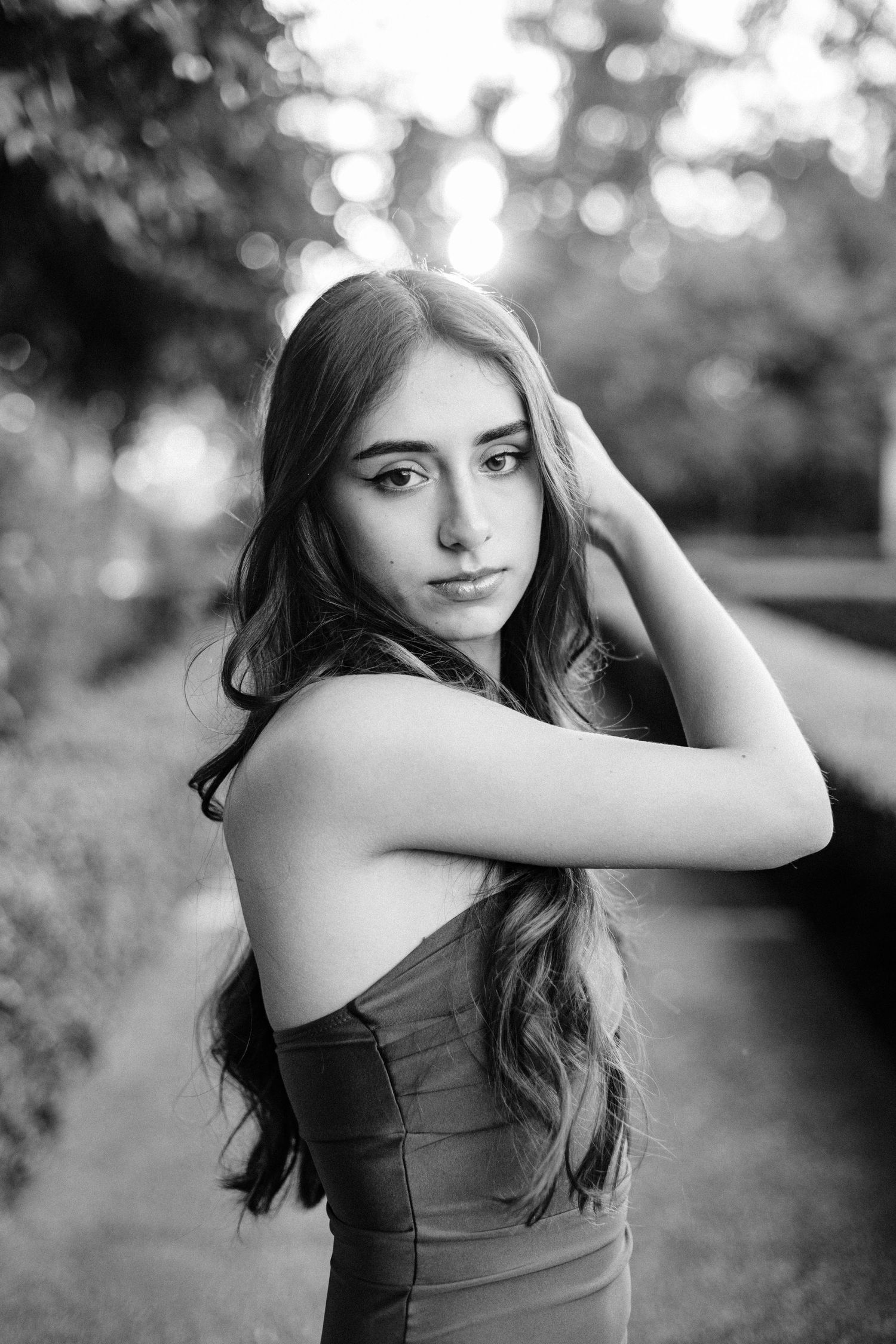 Black and white portrait of a young woman with long wavy hair posing outdoors in a strapless dress.