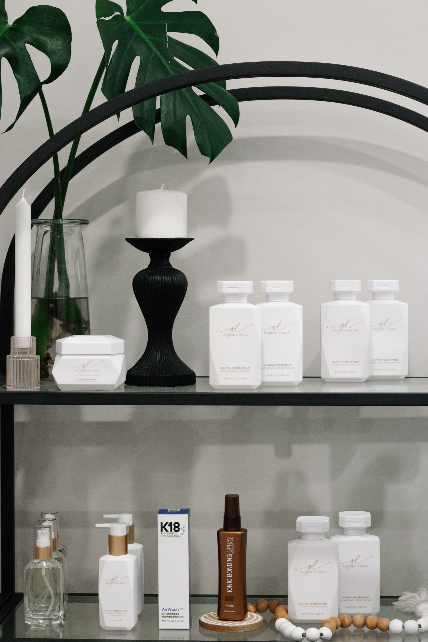 Modern salon suite shelf with monstera plant, candle holder and white beauty products.