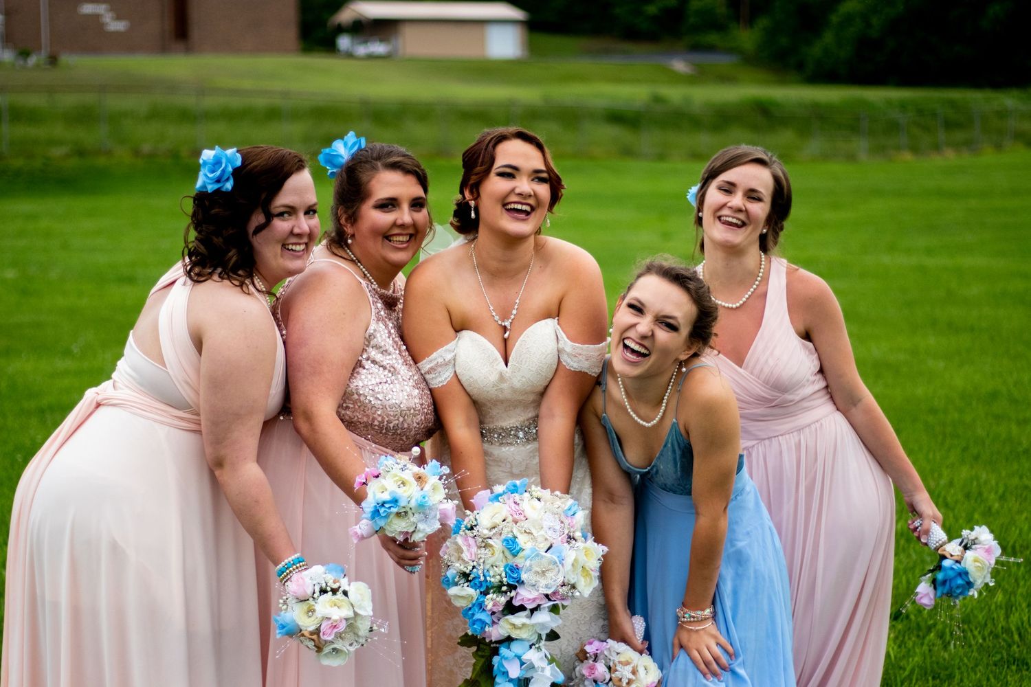 Bridesmaids in pink and blue dresses pose together on a green lawn.