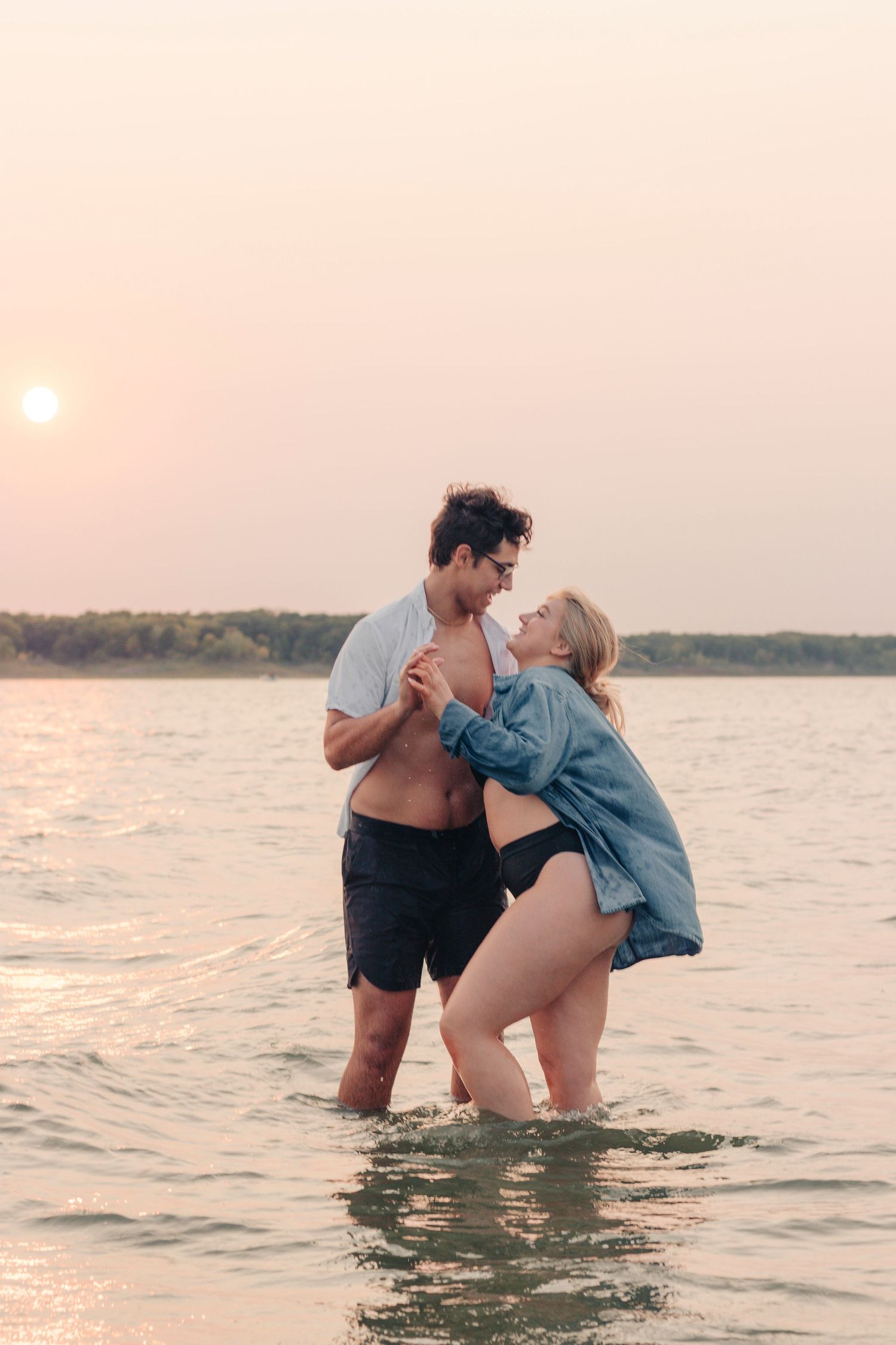 A couple plays in the water during sunset at the beach.