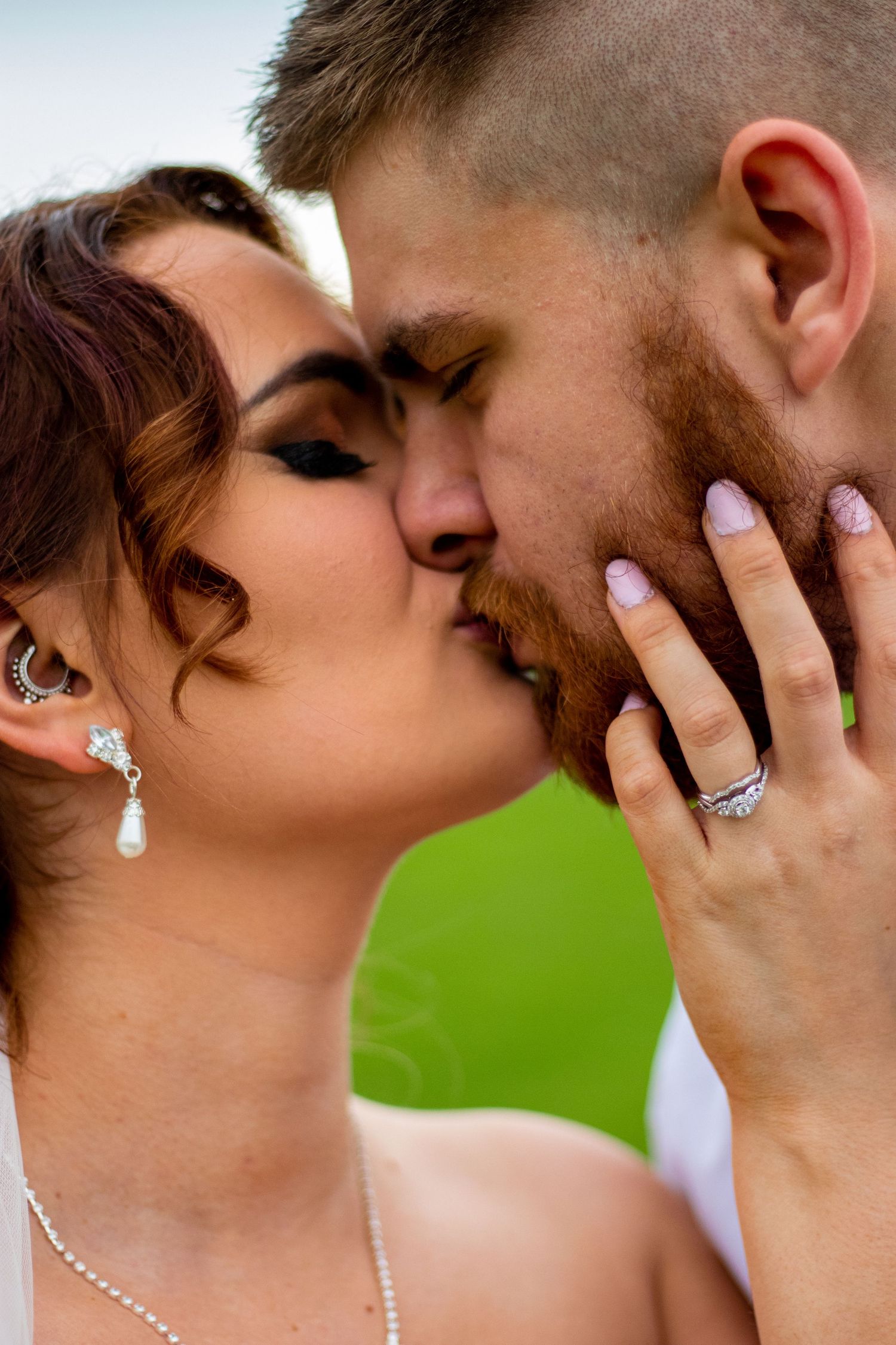 Intimate wedding portrait capturing tender kiss with engagement ring detail.