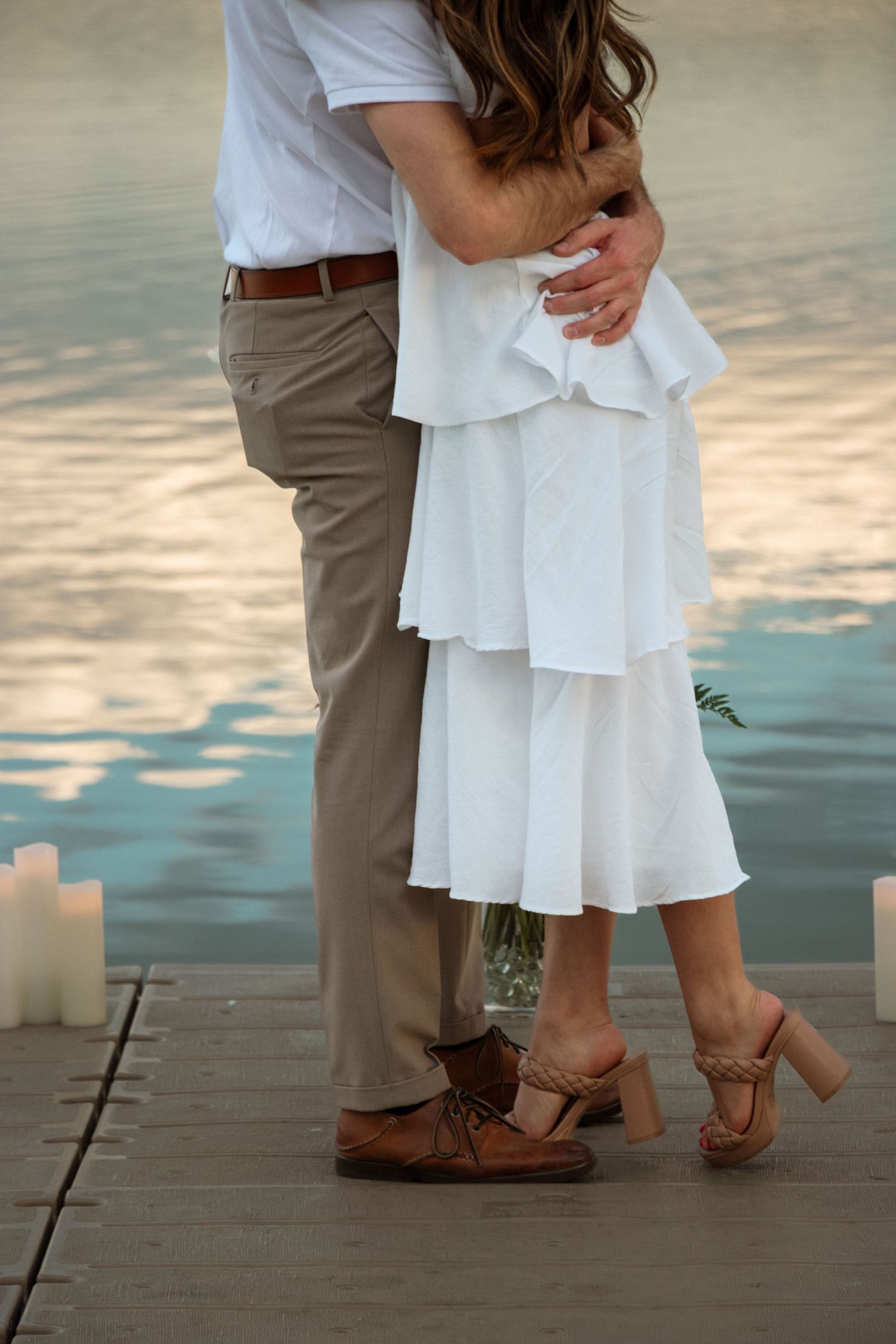 Close-up view of a couple's feet during a romantic sunset photoshoot on a wooden pier.