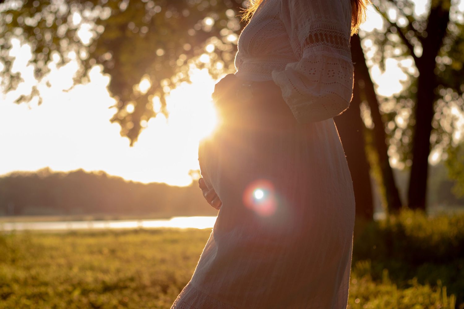 A silhouette of an expectant mother against a golden sunset by the water.
