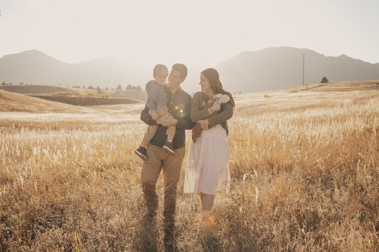 A family stands together in a golden wheat field at sunset with mountains in the background.