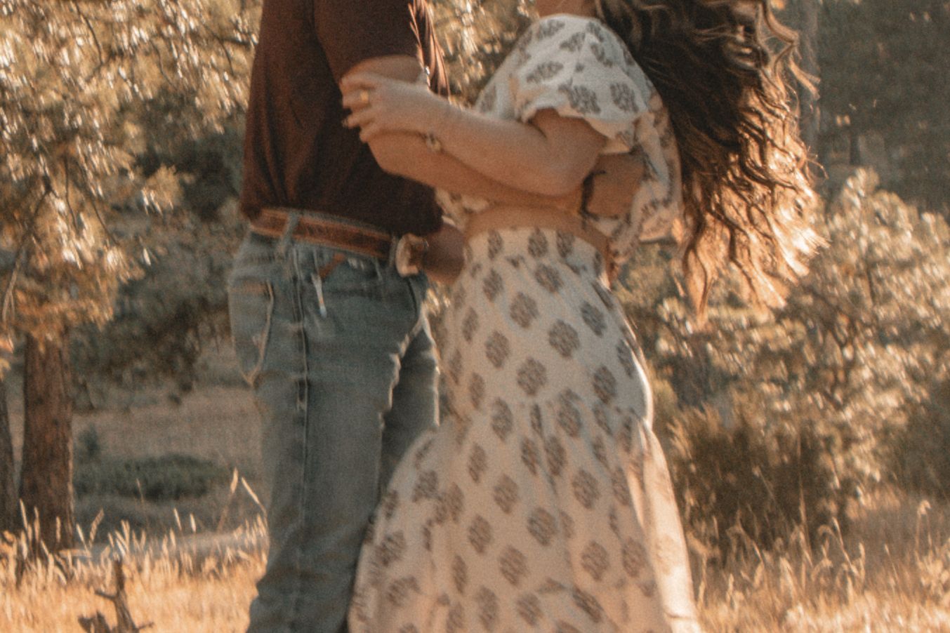 Couple in vintage attire dancing on a rustic hillside among tall pine trees.