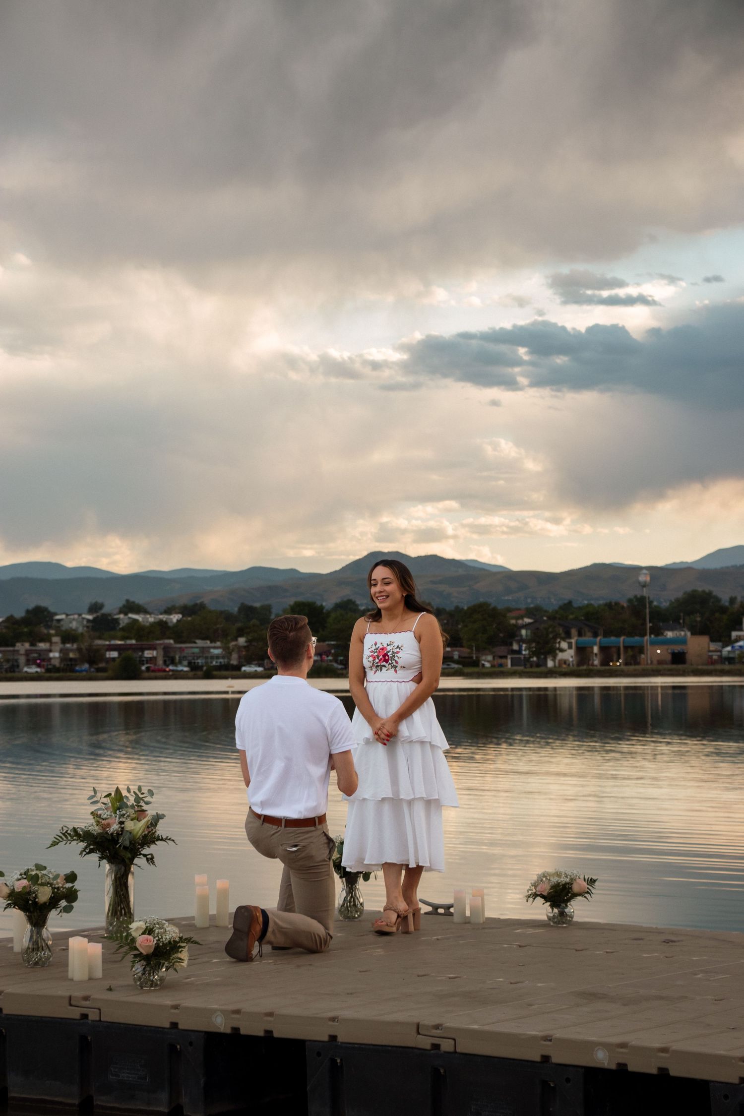 A romantic sunset photoshoot on a wooden dock by the lake with mountains in the background.