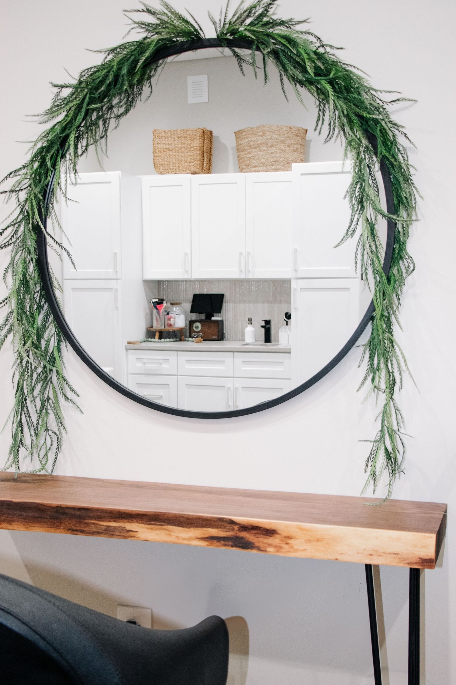 Modern interior design with black round mirror adorned with greenery above a rustic wood console table.