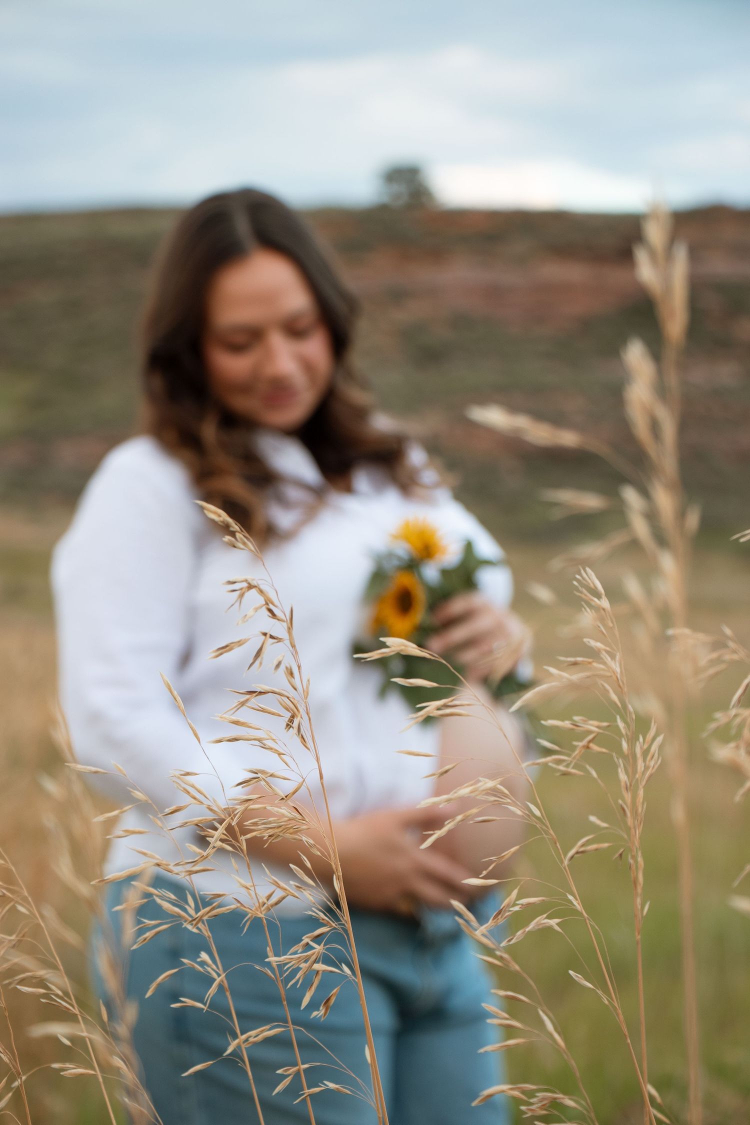 A person in a white sweater sits in a field of tall grass and dried wheat stalks with a vintage camera.