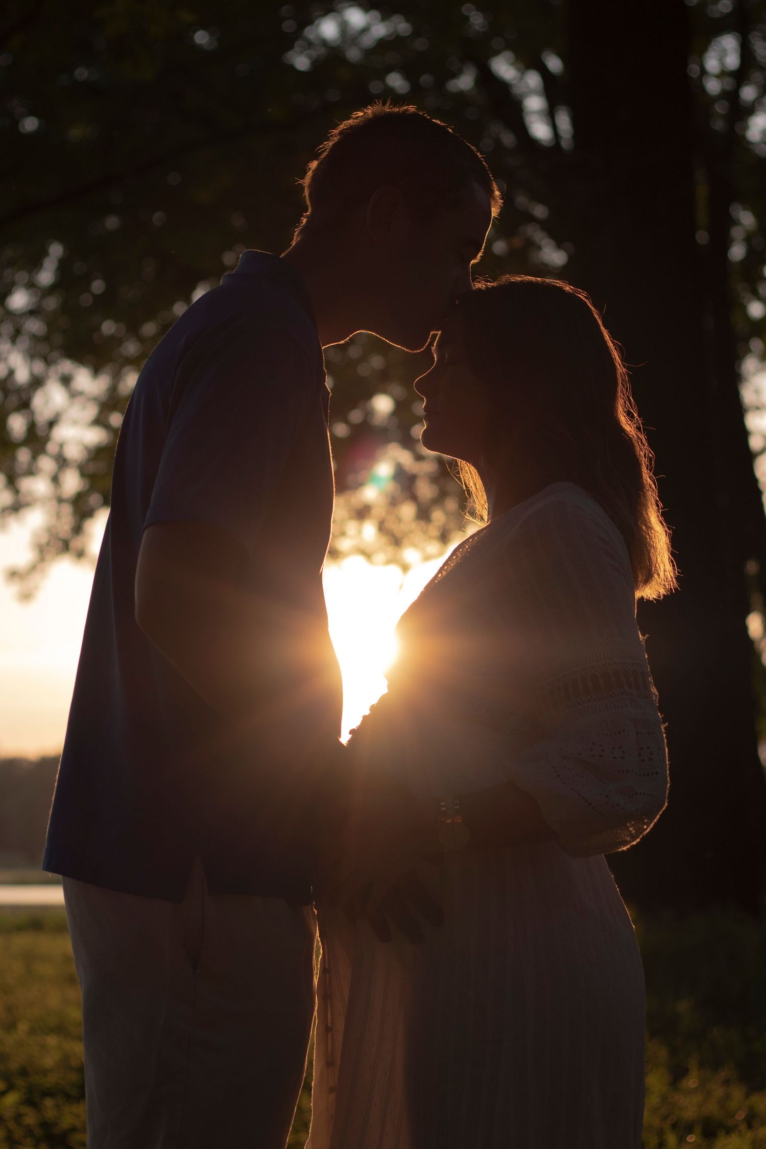 Silhouetted couple sharing an intimate moment at sunset in a grassy field.