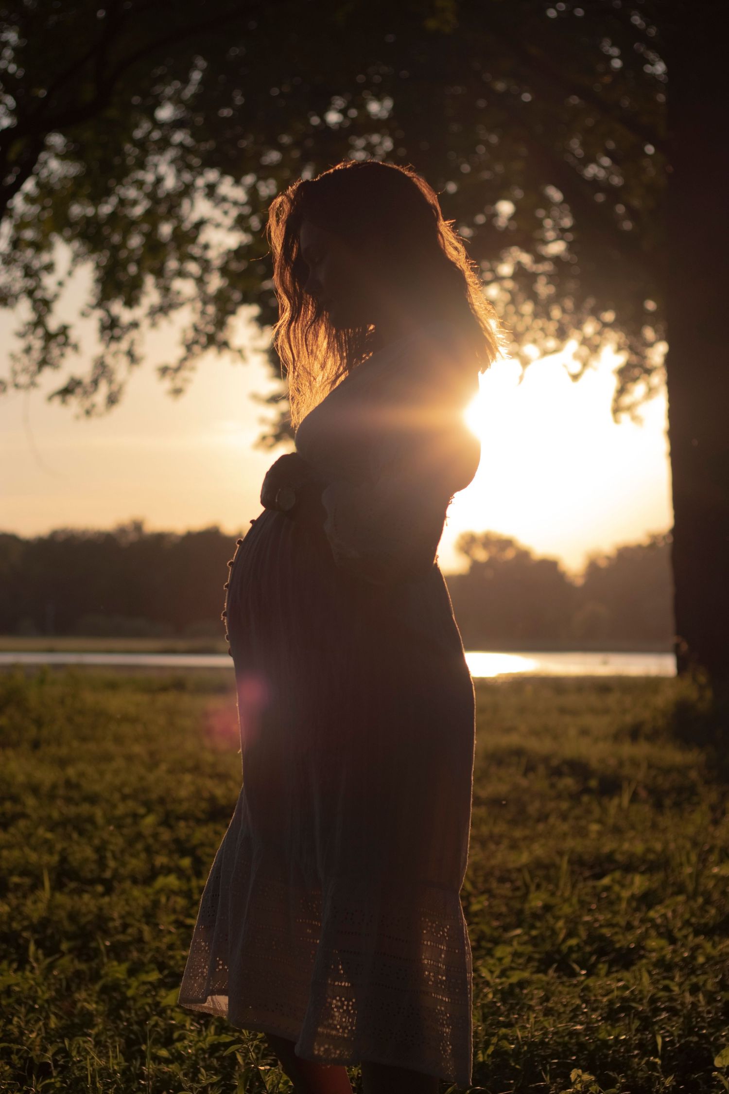 Silhouette of person standing by lake during golden hour sunset.