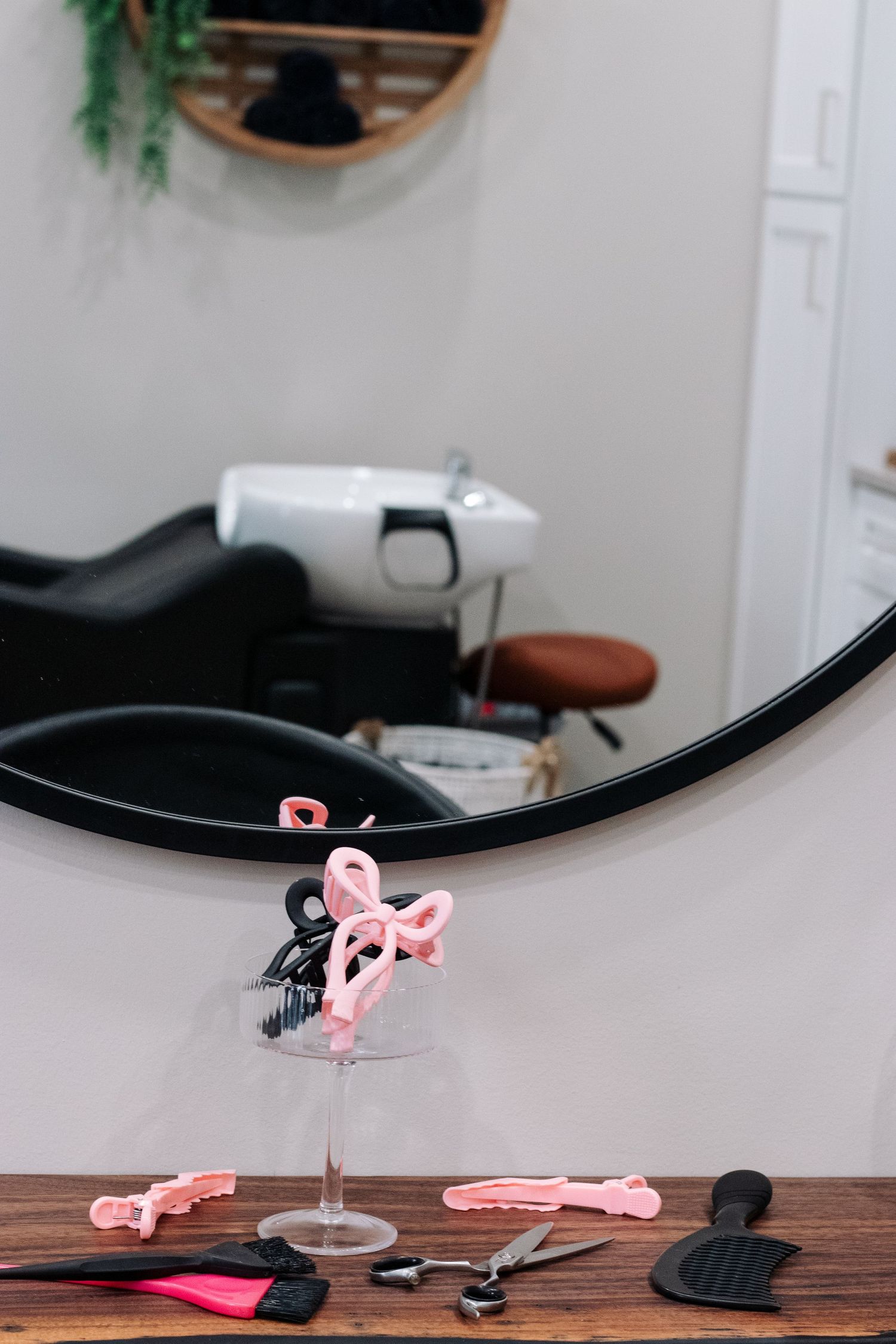 Pink hair accessories and styling tools arranged on wooden surface with black mirror frame.