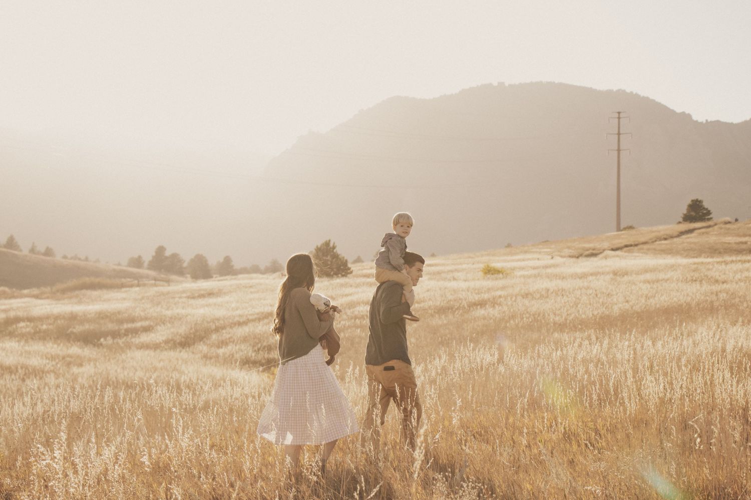 Couple standing together in a golden wheat field at sunset with mountains in background.