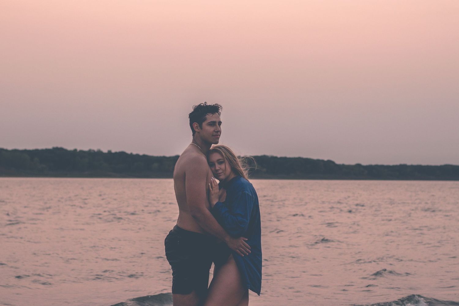 Couple standing in water embracing during pink sunset at lake.