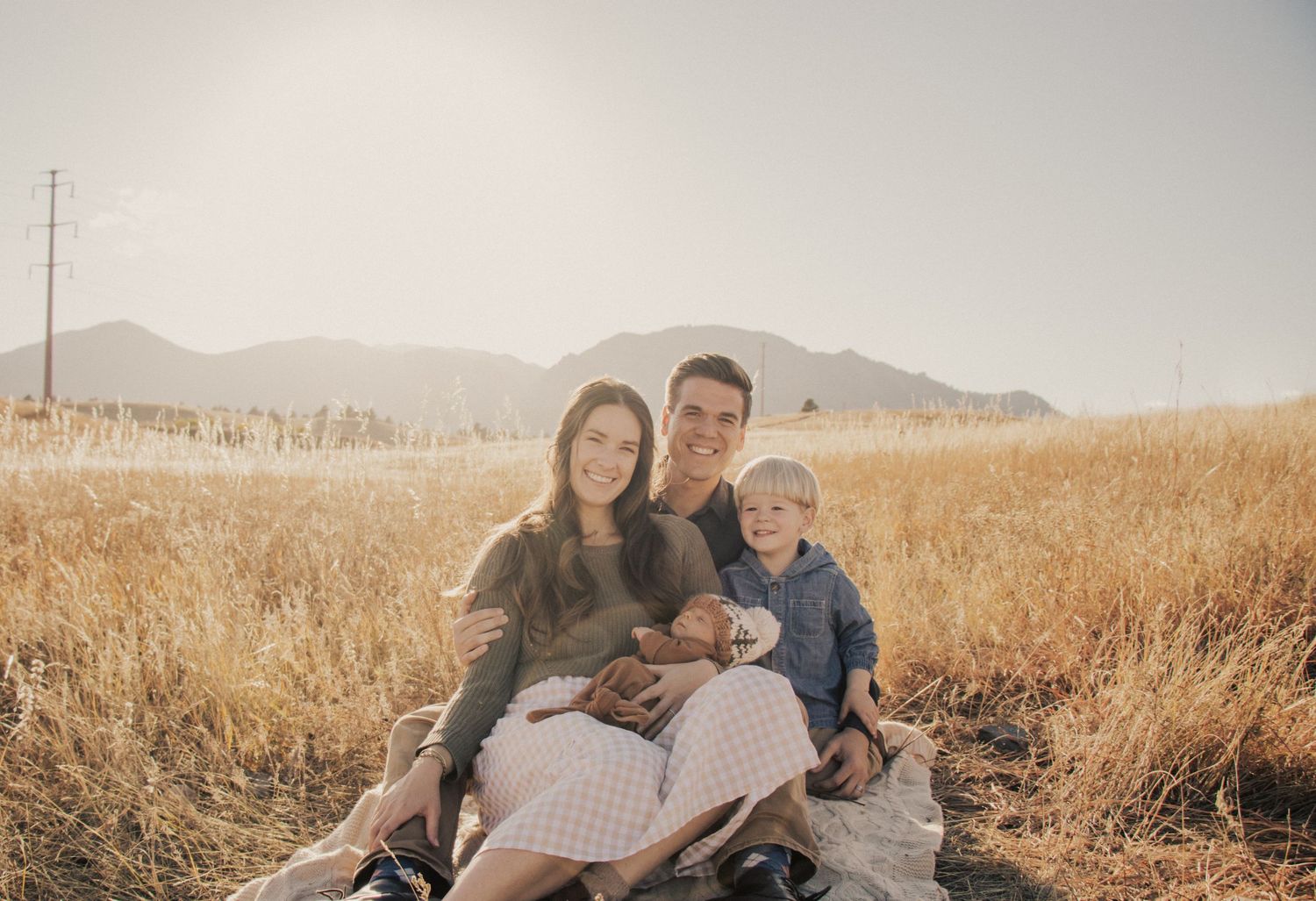 Family sitting together in golden field with mountains in background.