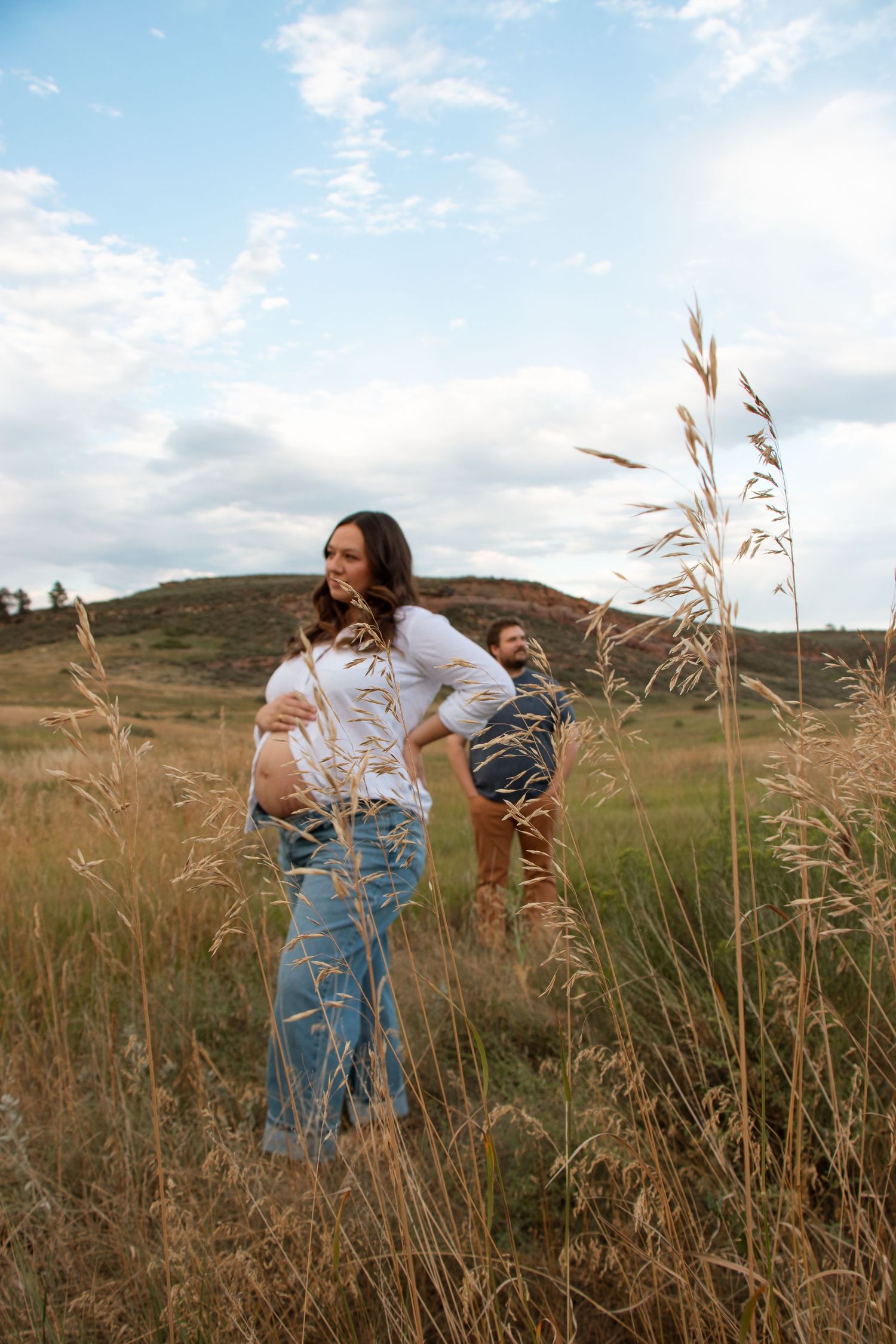 Couple embraces in golden field of tall grass during sunset in rustic countryside setting.