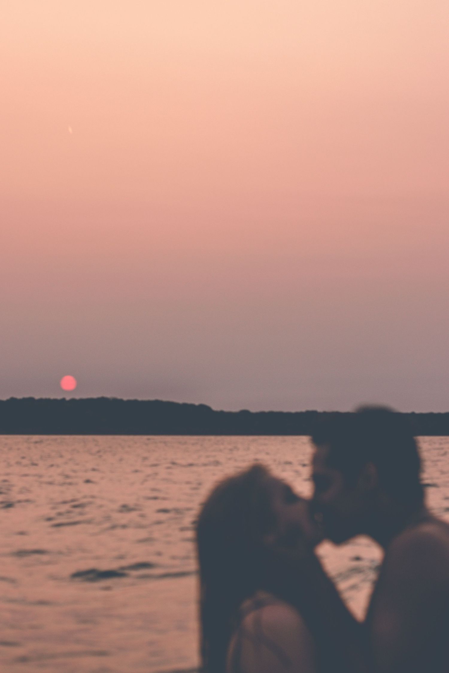 Silhouetted figures embracing in water against pink sunset sky.