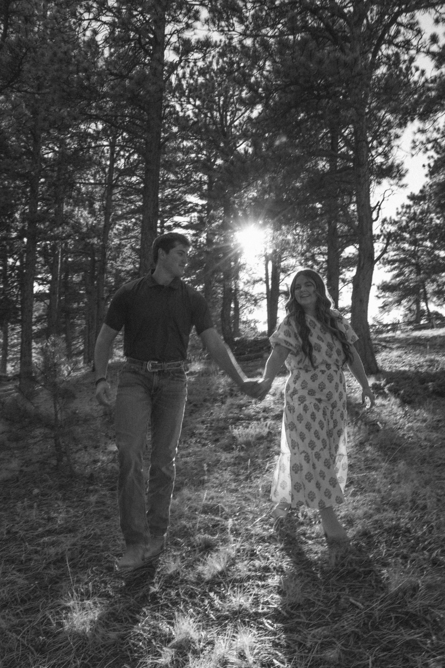Couple in wooded area with dramatic sunburst through pine trees.