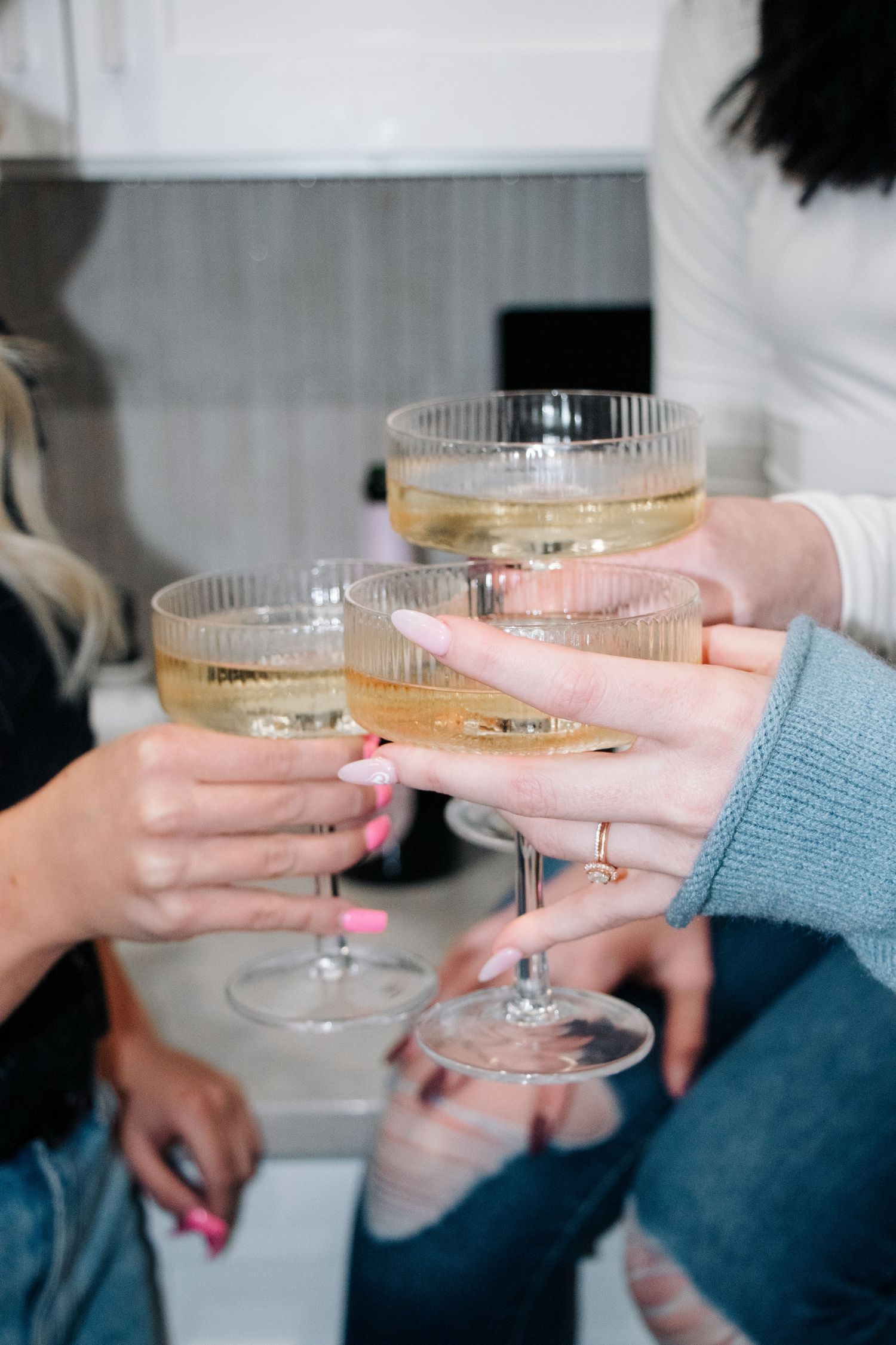 Several hands raise champagne coupe glasses filled with sparkling wine for a celebratory toast.