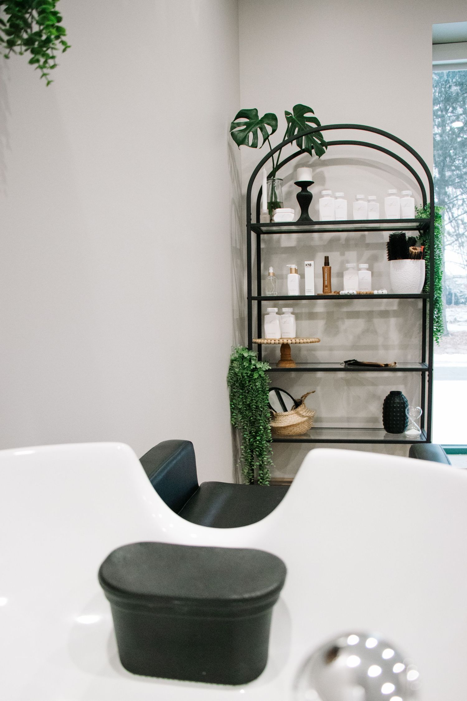 Modern salon interior with arched shelf unit displaying products and decorative plants.